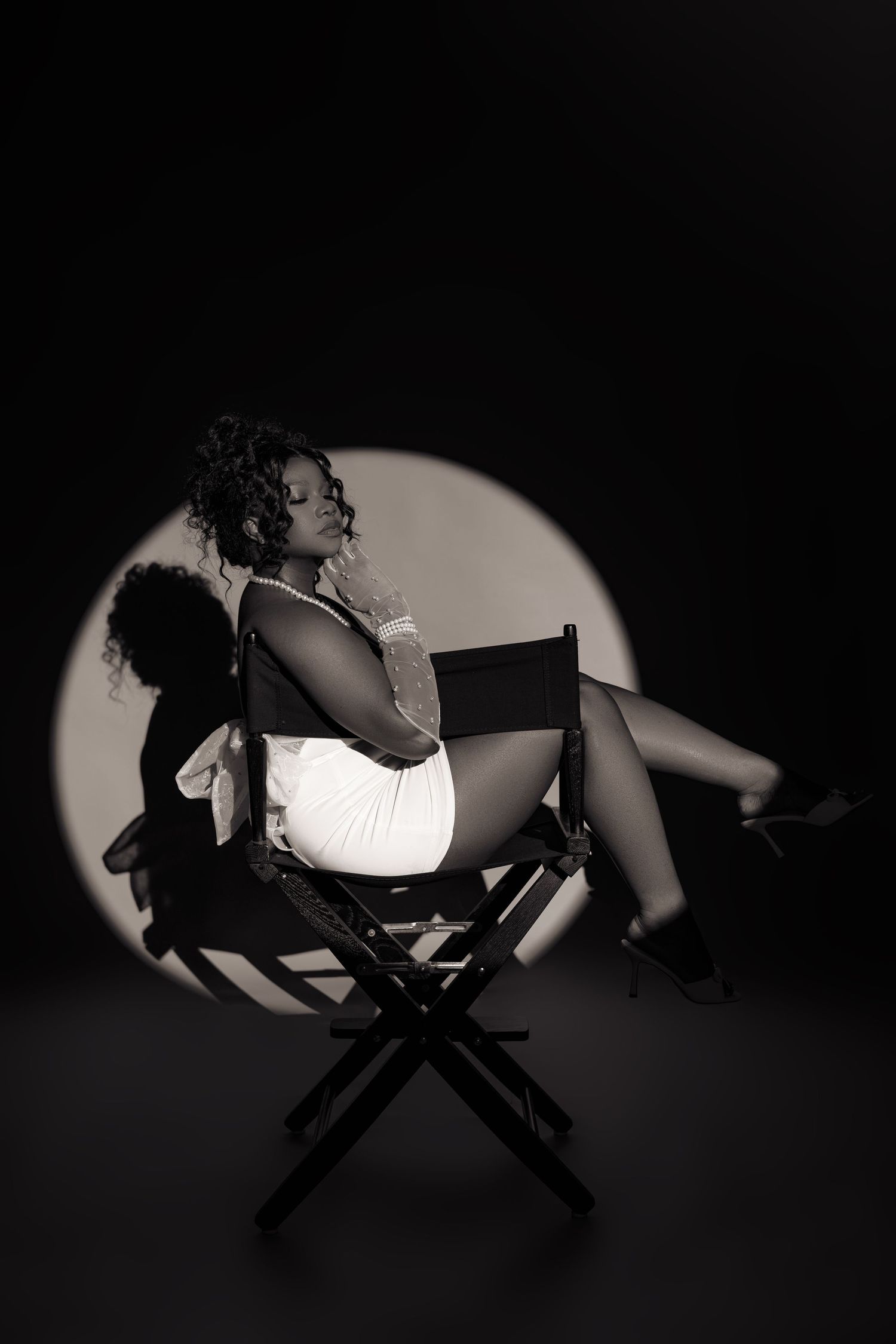 A dramatic black and white photo series shows a figure in white seated on a director's chair casting dynamic shadows.