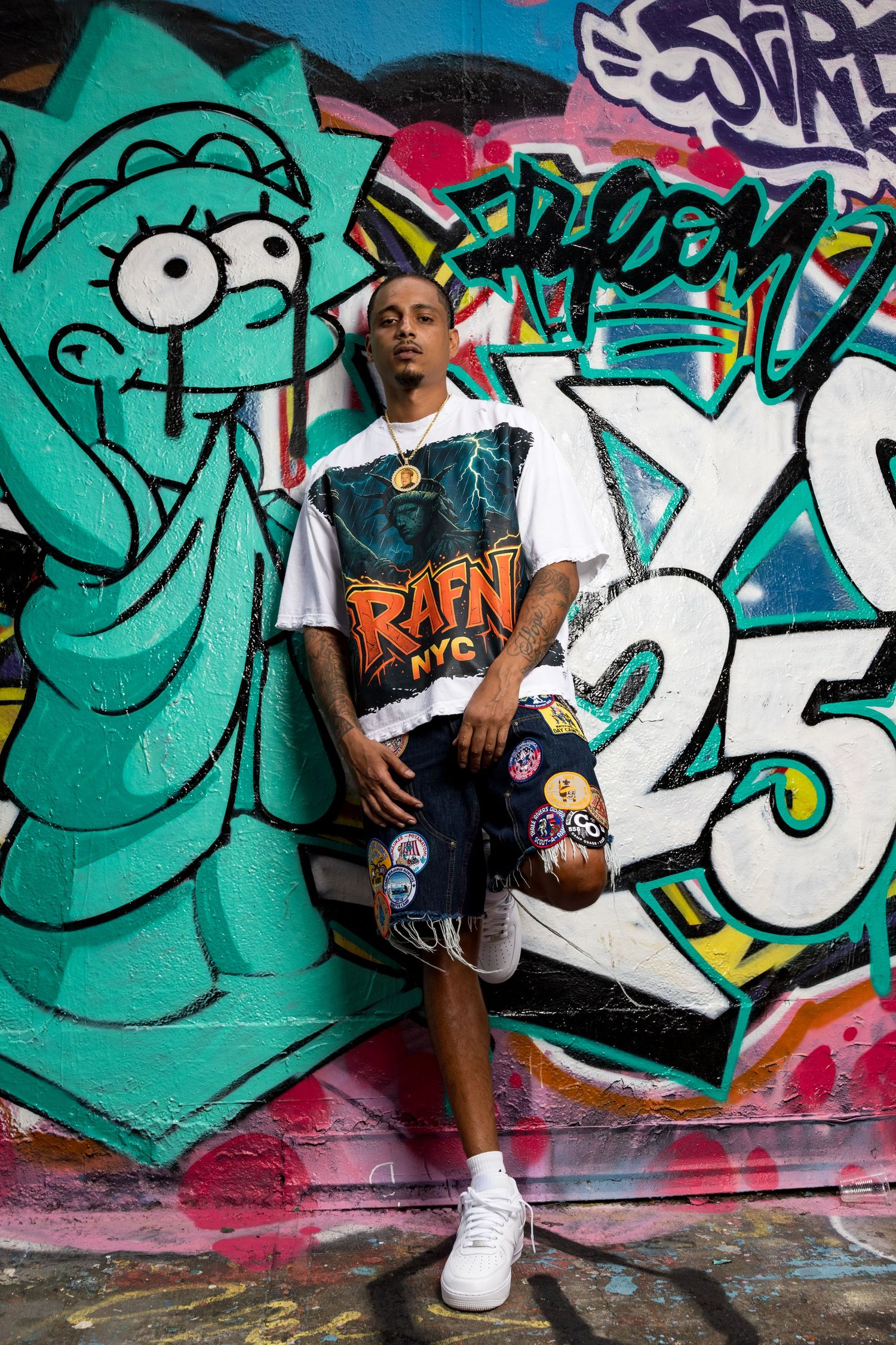Urban street art photoshoot featuring colorful graffiti with teal and white designs on a wall.