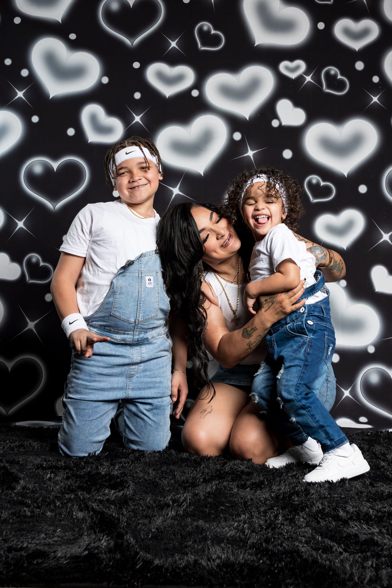 Family portrait session against black background with floating heart overlays and denim overalls.