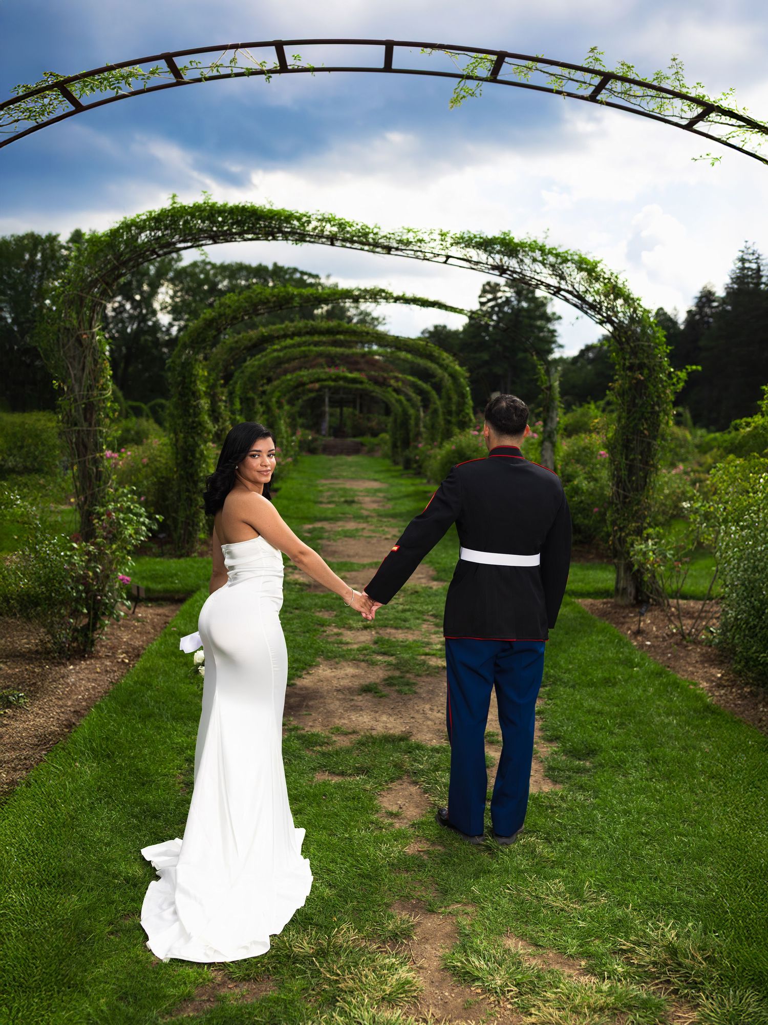 Couple poses under garden archway covered in vines during outdoor photo session.
