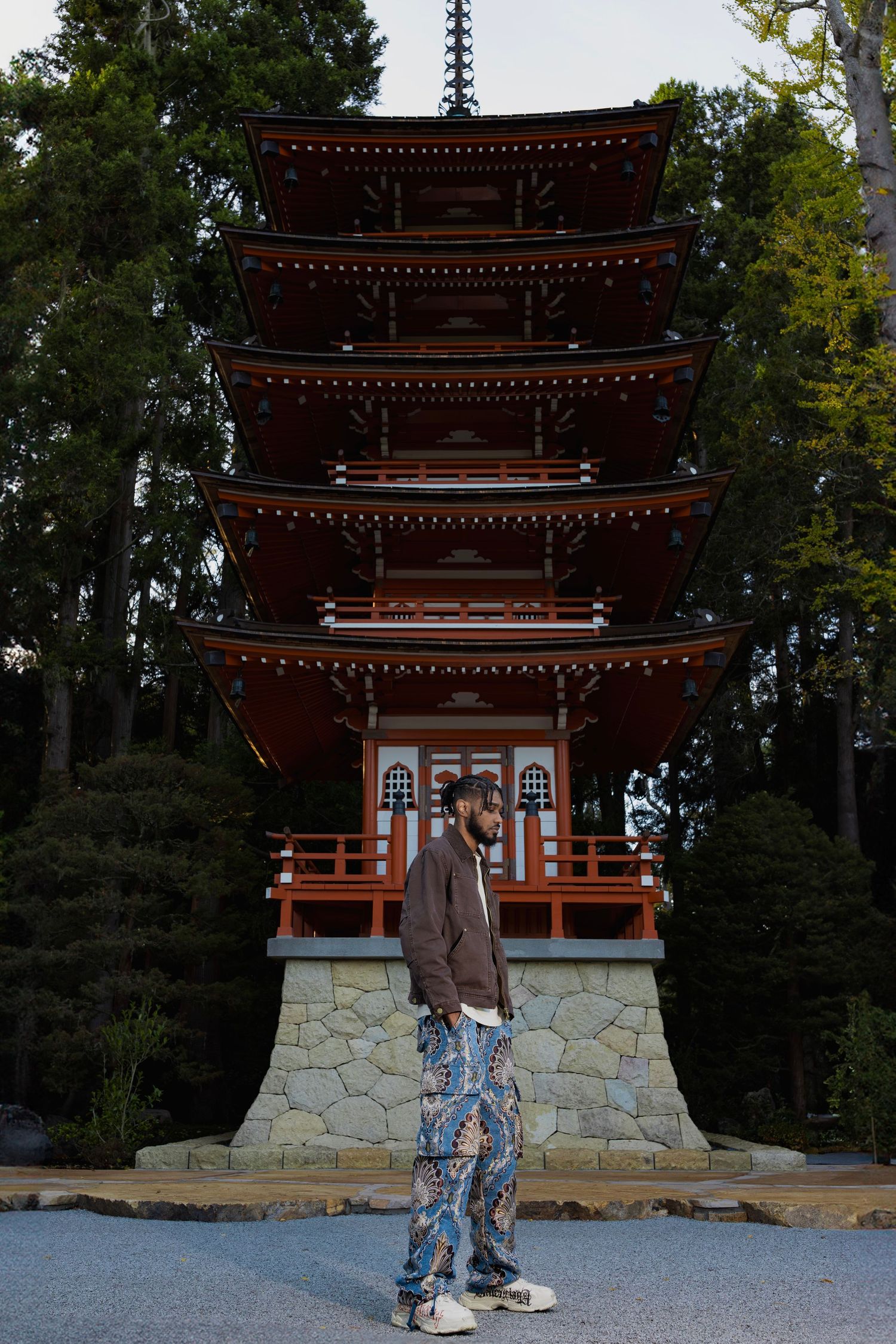 A traditional Japanese pagoda with red-orange tiers stands among trees in a serene garden setting.