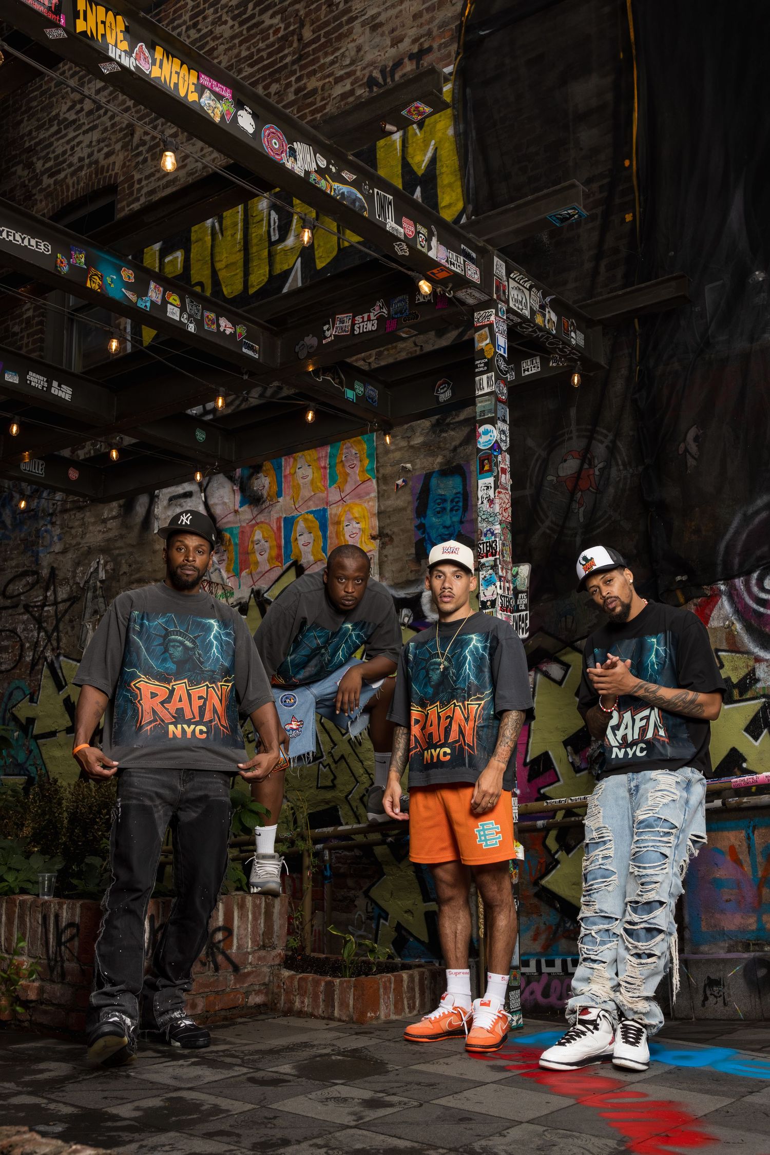 Group of hip hop artists pose in urban setting with graffiti walls and street style fashion.