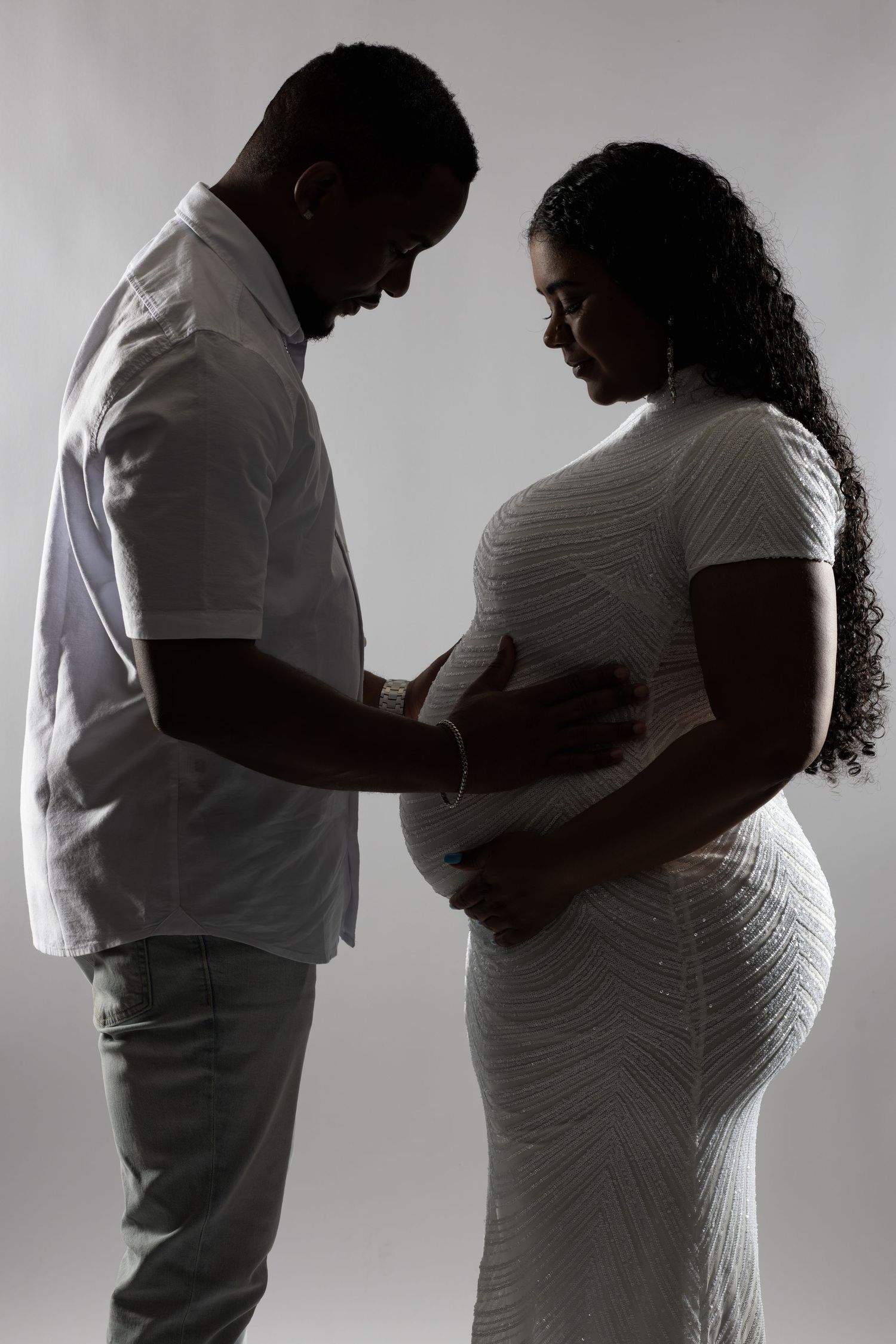 Silhouette series showing tender moments between expectant couple in white against grey background.