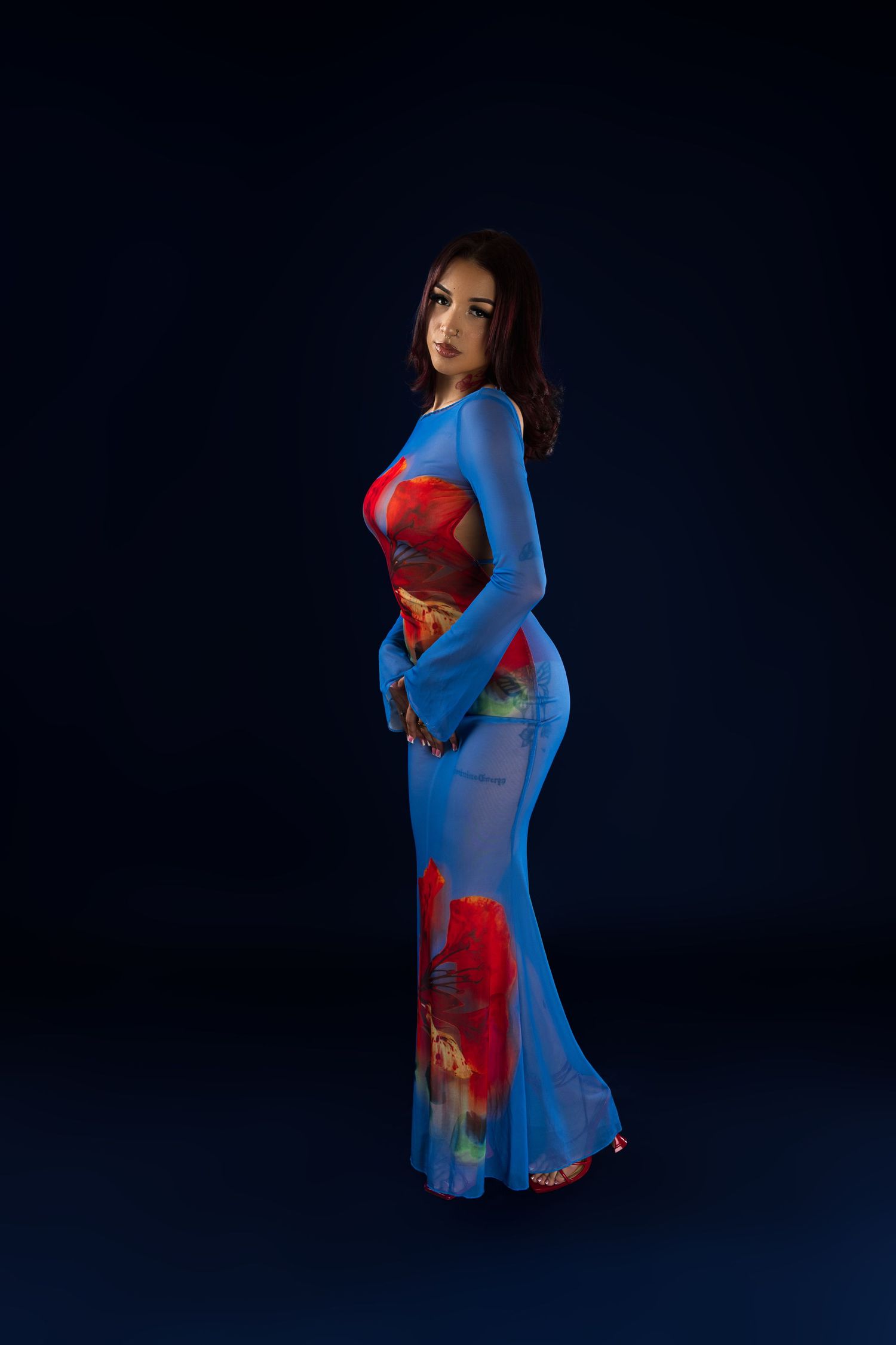Fashion model poses in a flowing blue and red dress against dark background in artistic photo series.