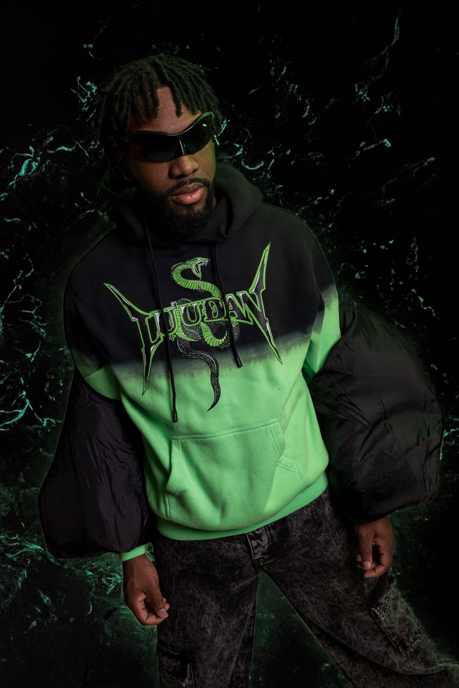 Person wearing neon green and black hoodie in dark atmospheric setting.