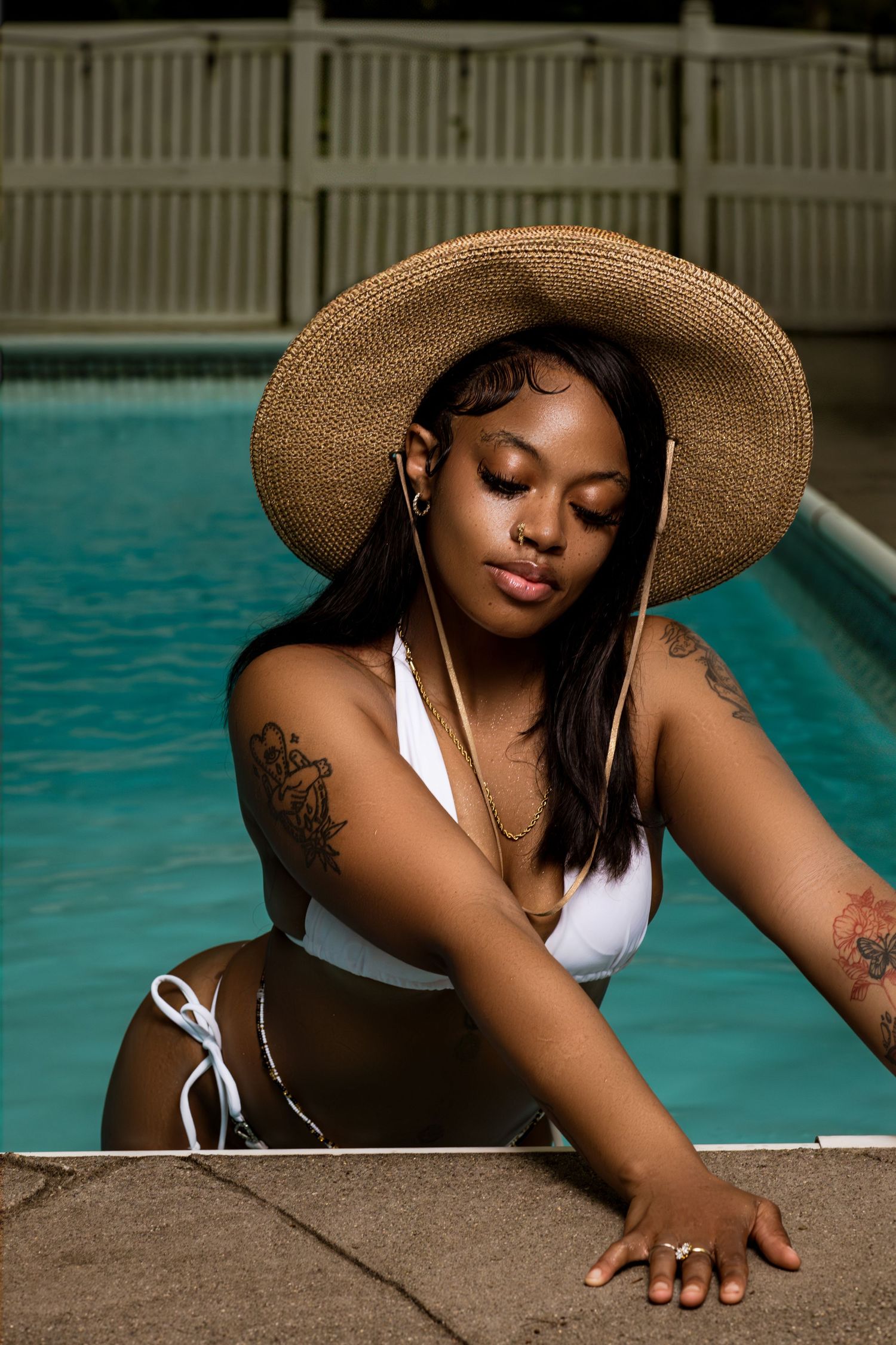 Poolside photoshoot with a wide-brimmed sun hat and white swimwear against turquoise water.