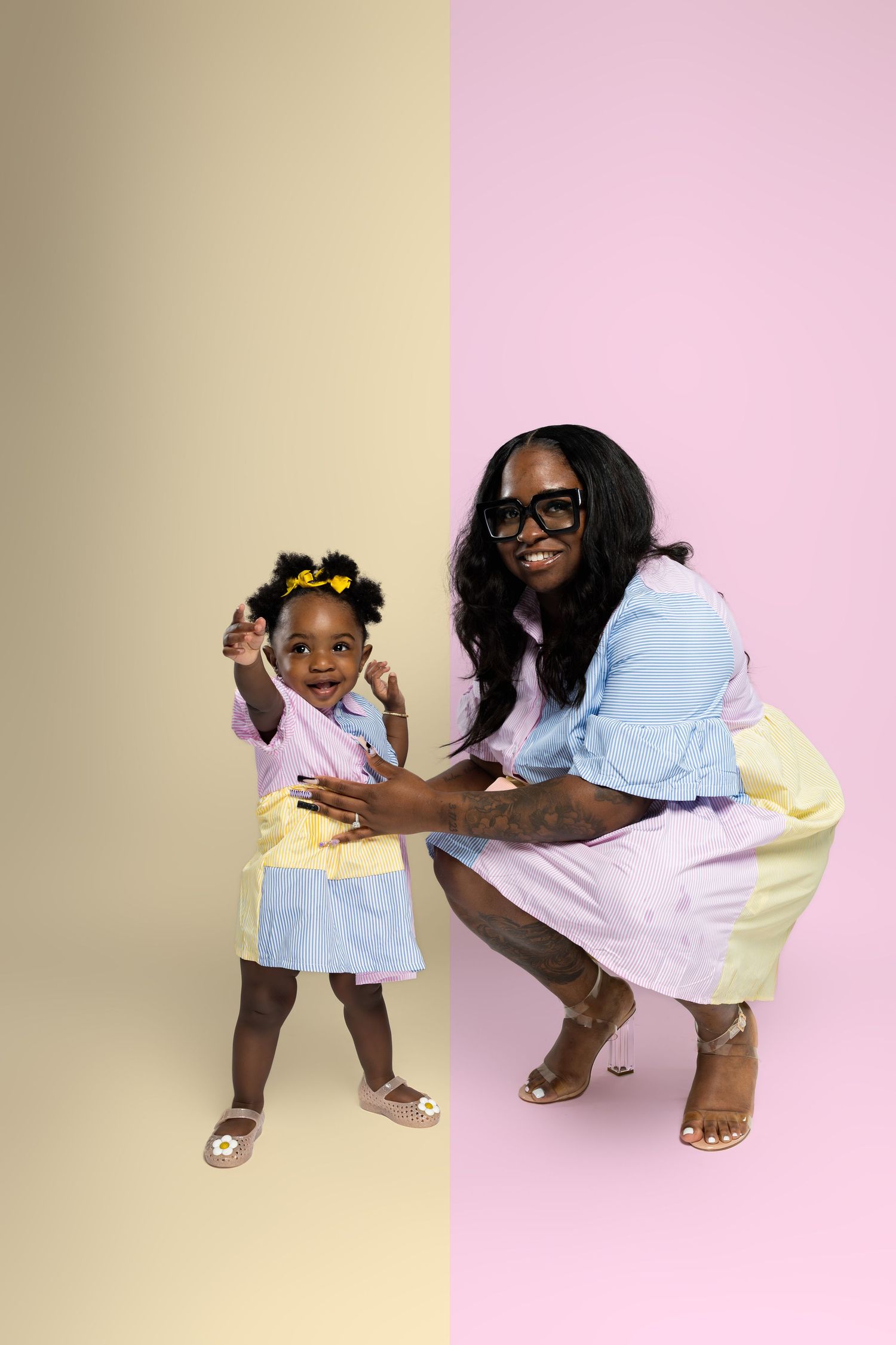 Two people in matching white and yellow outfits pose playfully against a pink and yellow background.