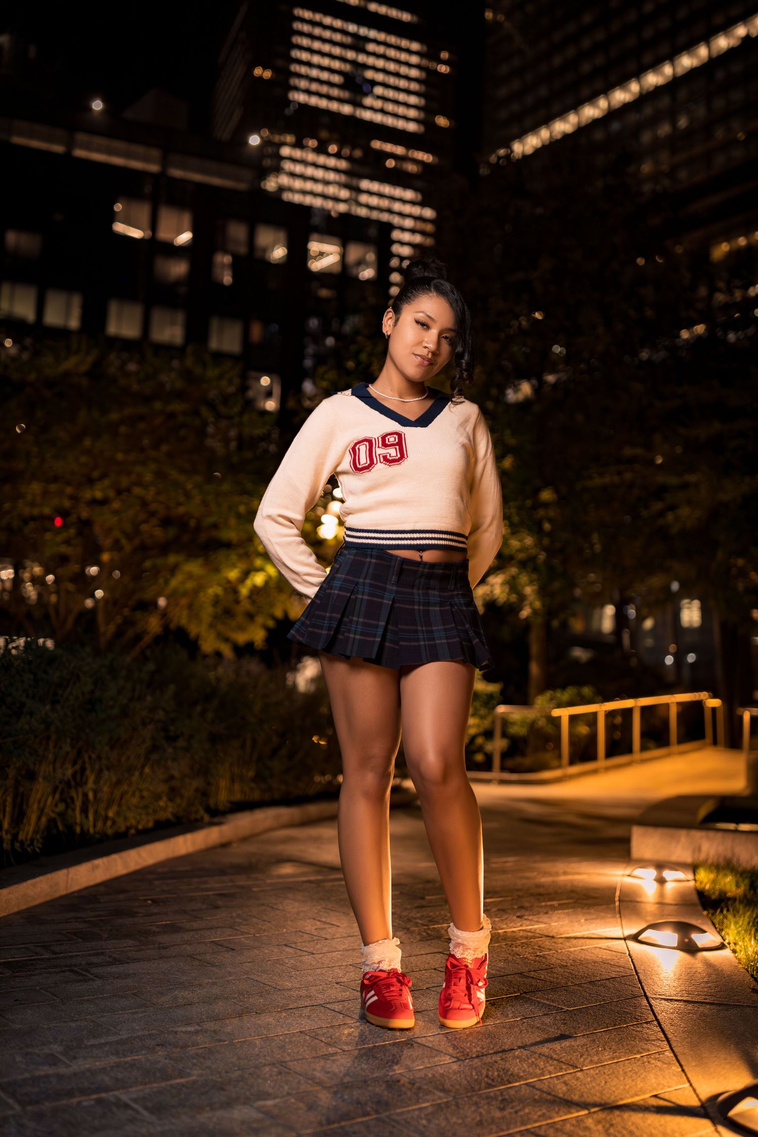 Nighttime fashion shoot featuring sporty outfit and red sneakers against city backdrop.