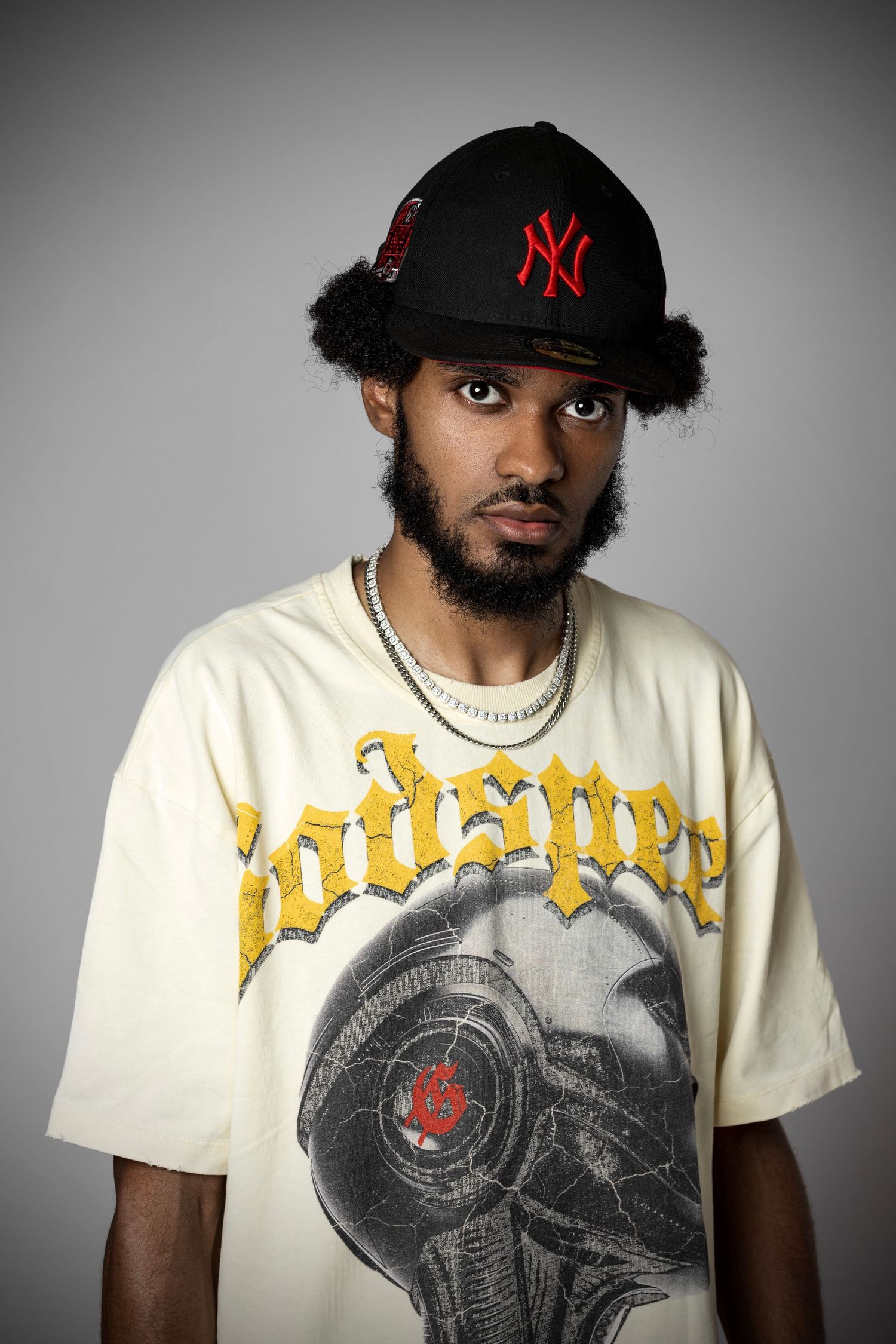 A series of photos showing someone wearing a New York Yankees cap and vintage-style graphic t-shirt against a gray backdrop.