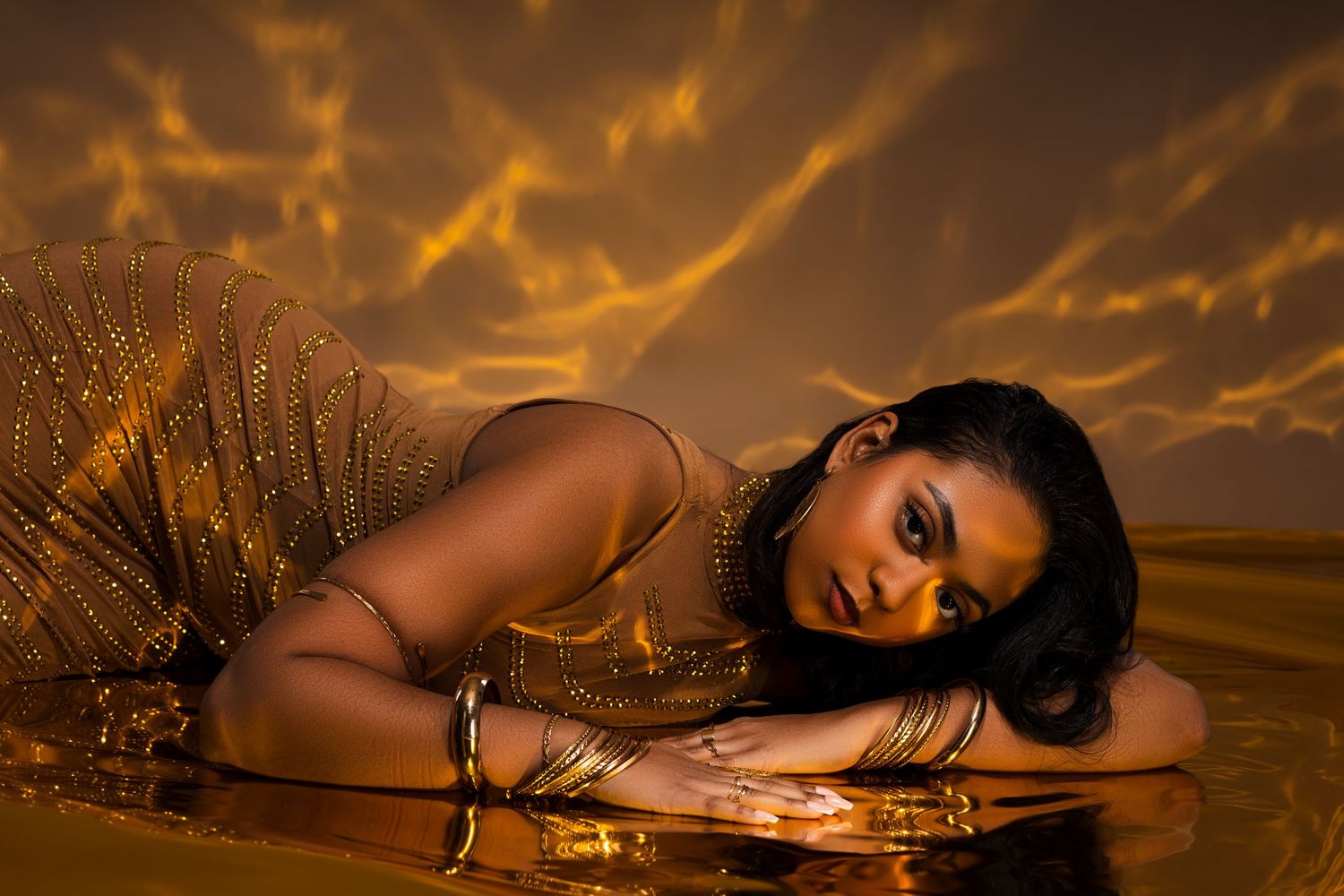 Glamorous fashion portrait with golden lighting and reflective surface creating ethereal mood.