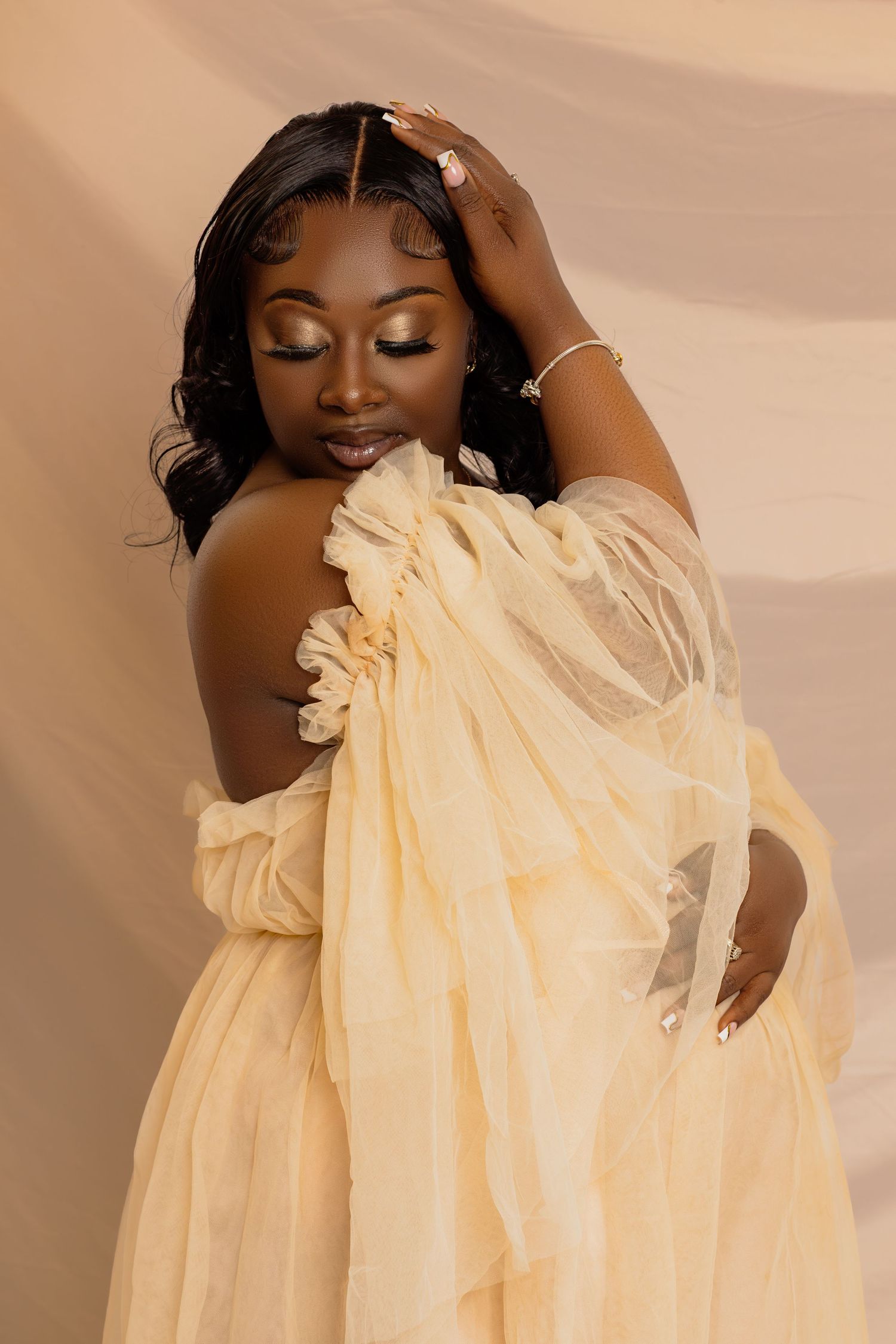 Artistic maternity photoshoot featuring flowing cream fabric against warm neutral background.
