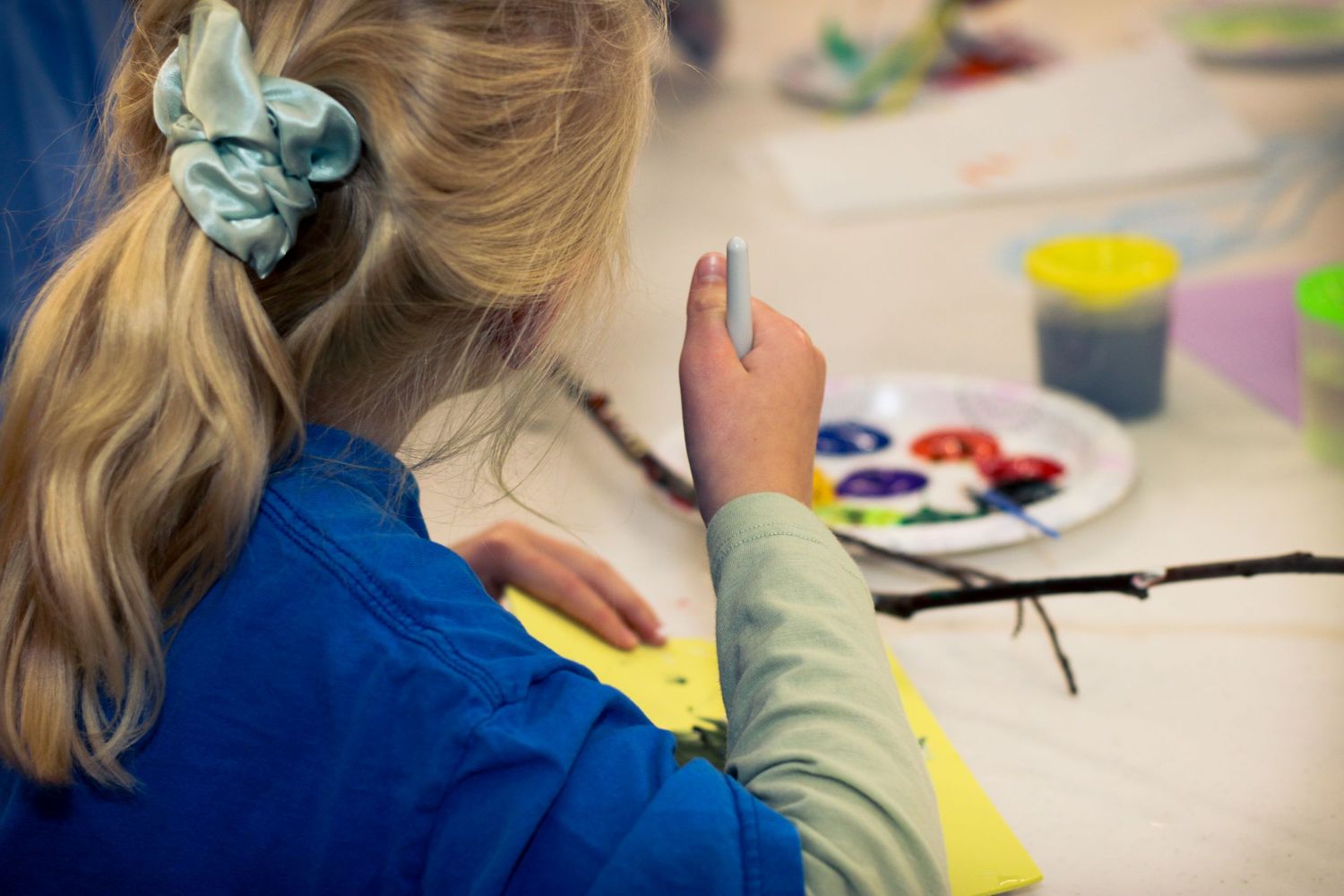 Children work on colorful art projects at a table with paint and art supplies during a creative activity session.