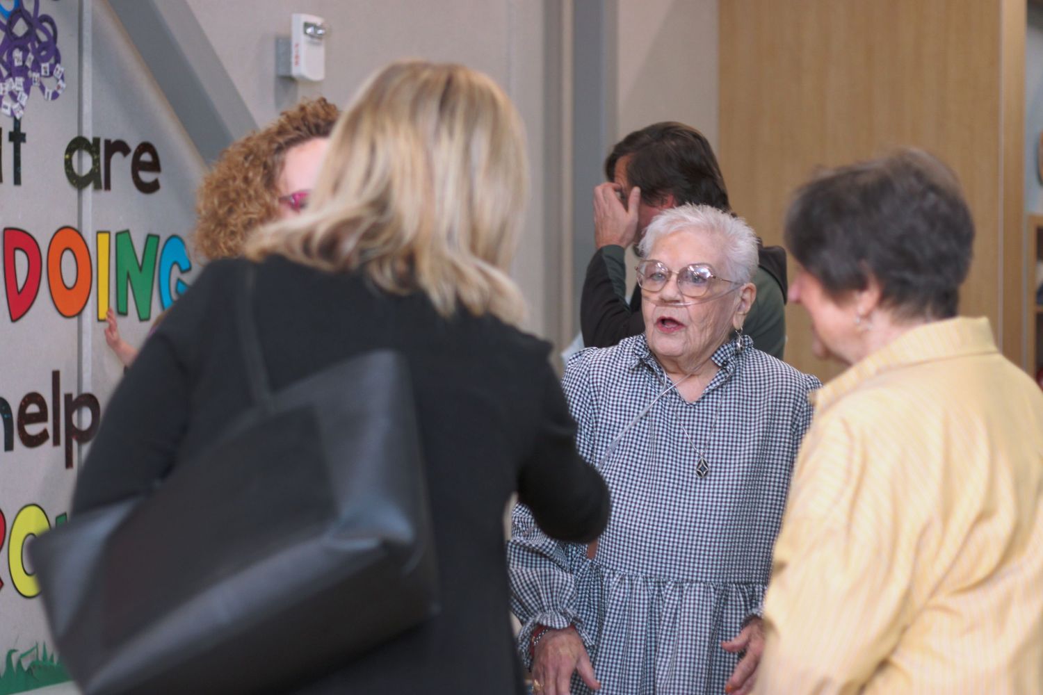 A group of seniors participate in a lively activity session in a community center with colorful decorations on the wall.