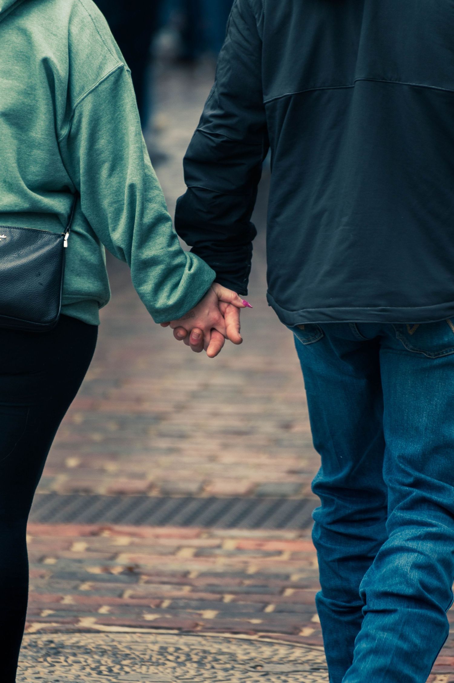 Close-up view of two people walking together on a brick paved street wearing jeans and casual jackets.