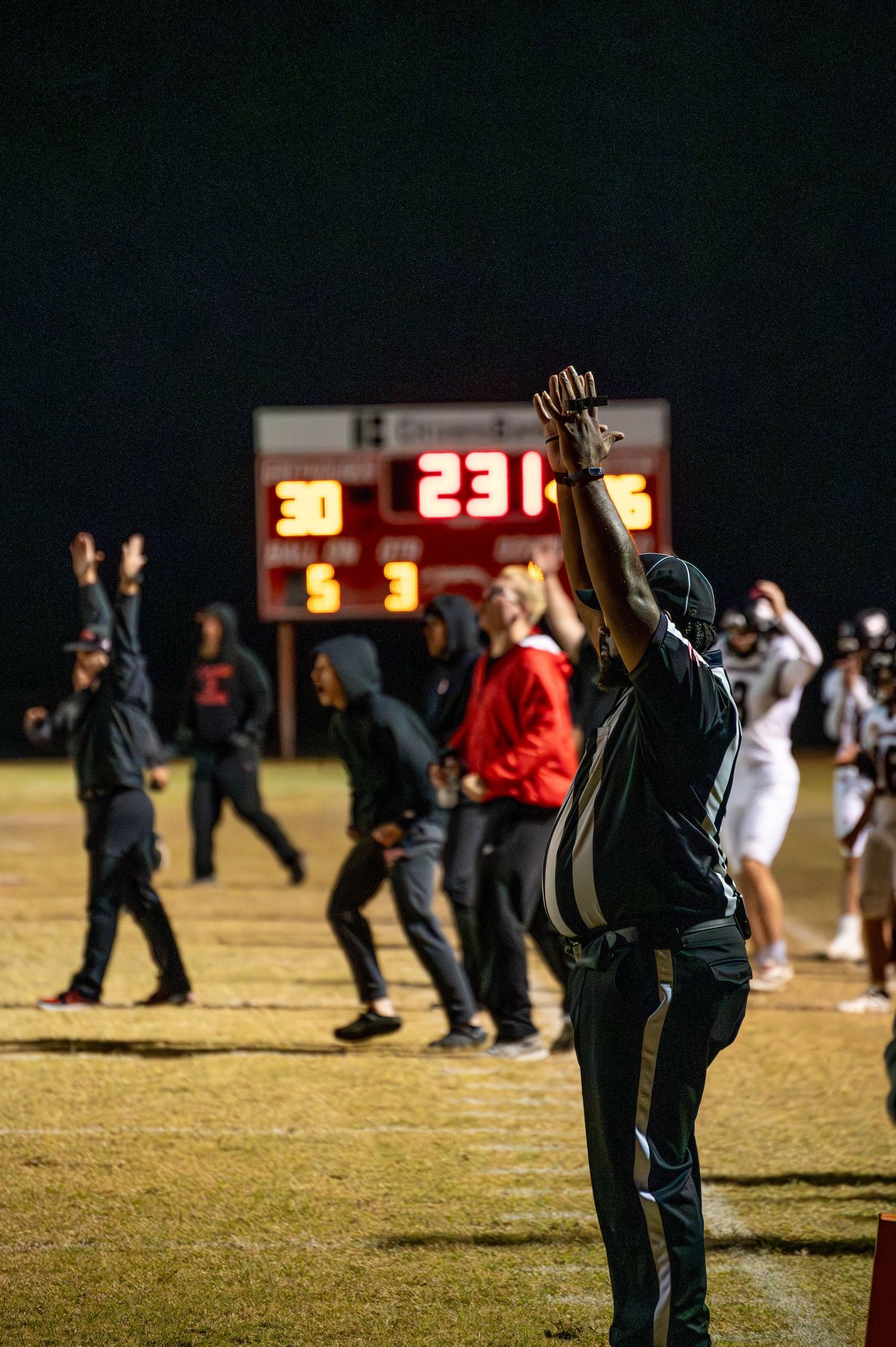Silhouette of a person raising their arm at a nighttime sports event with scoreboard glowing in the background.