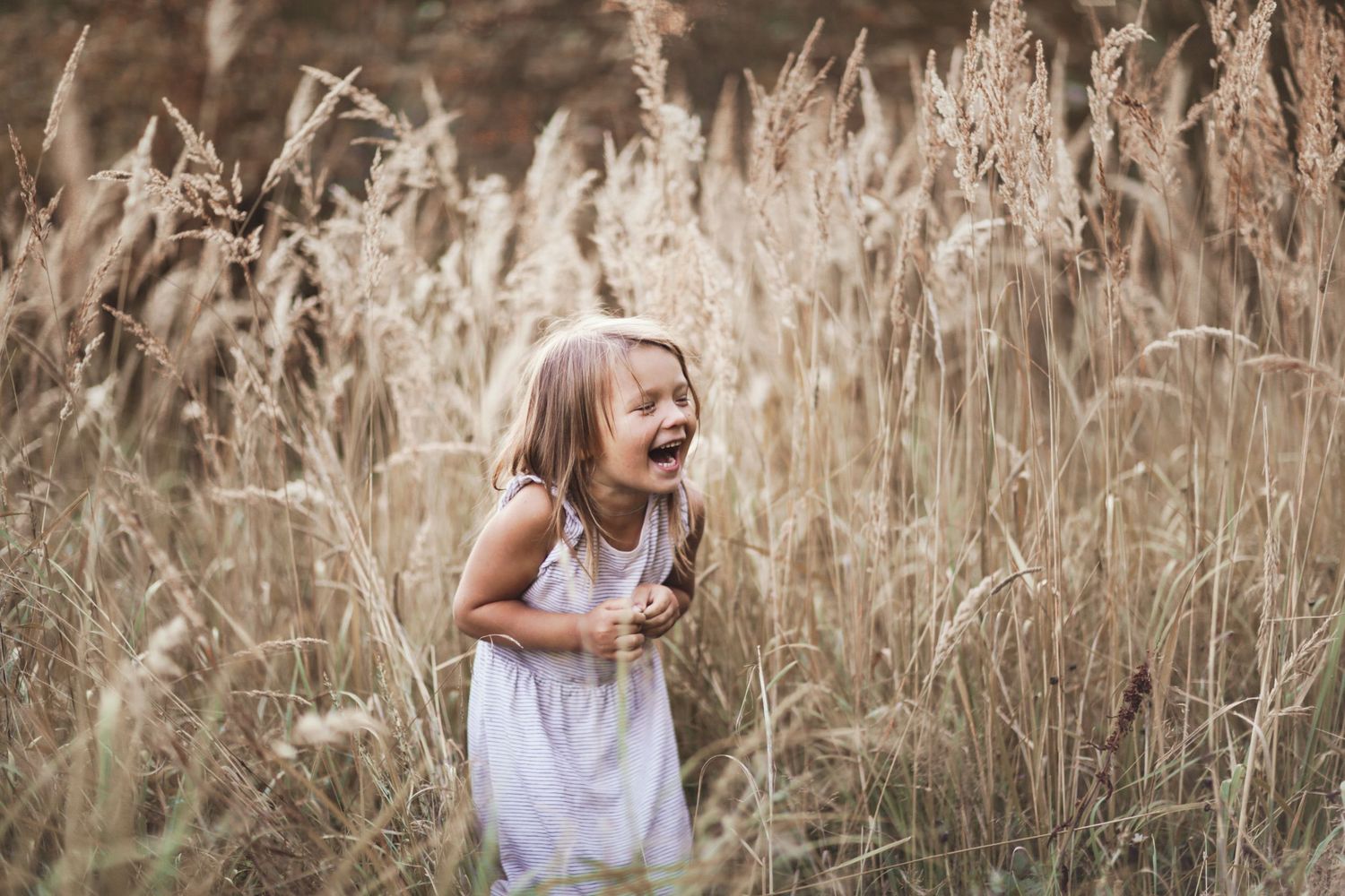 A person in a white dress runs joyfully through a field of tall golden wheat at sunset.