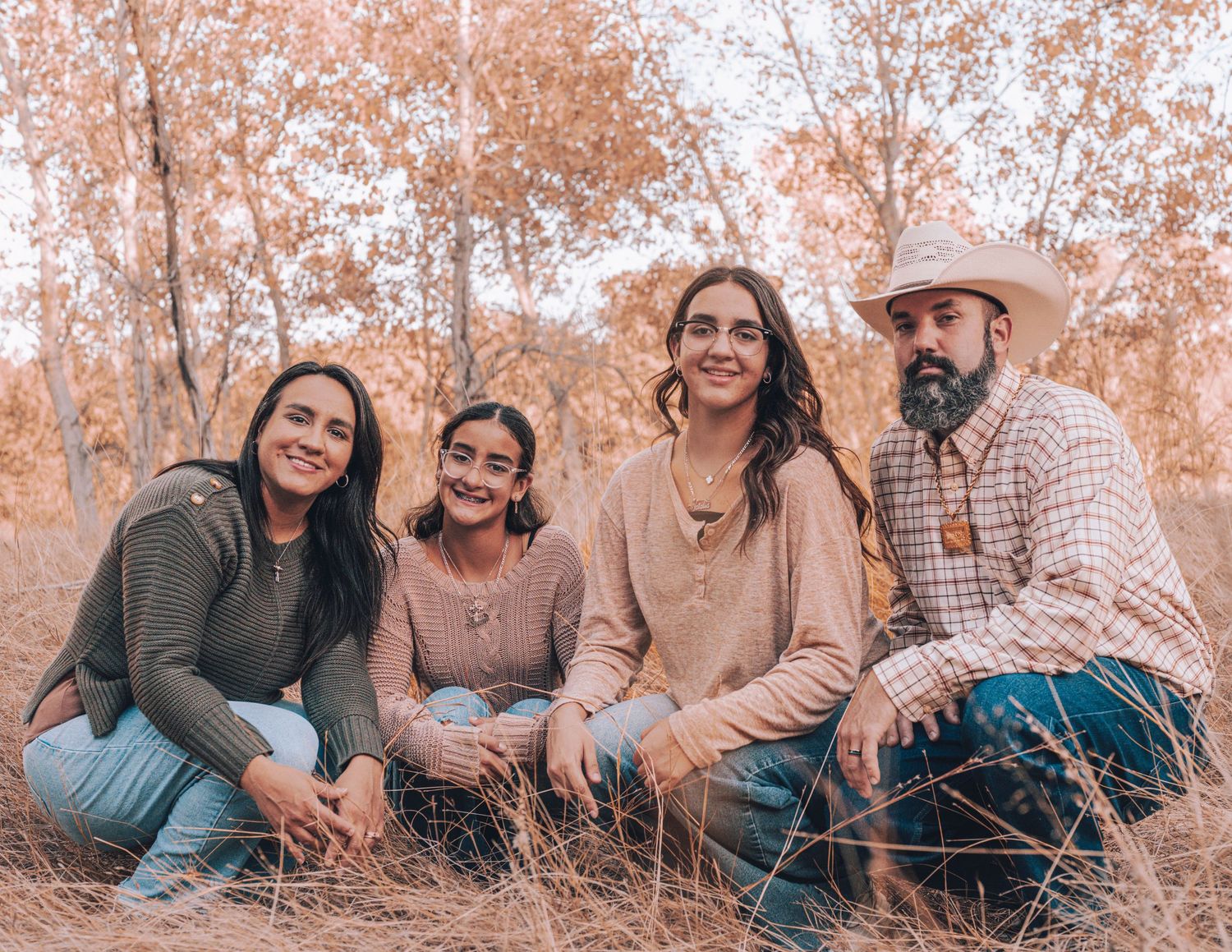 A group sits together outdoors with warm orange tones and fallen leaves in a casual outdoor portrait setting. Azle family photo session.