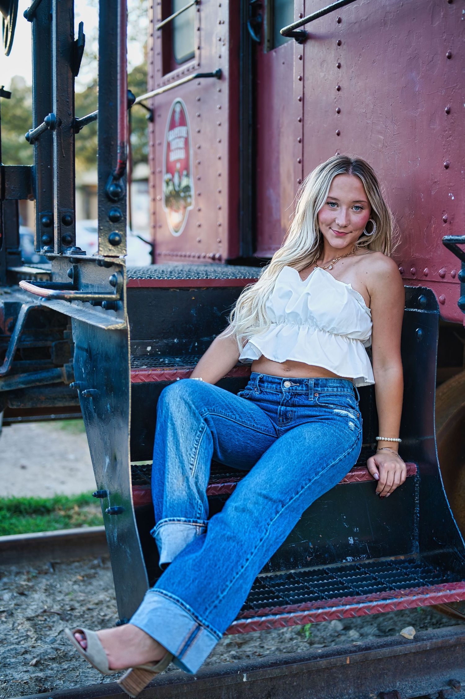 A casual outdoor portrait against a red train car relaxed poses in blue jeans and white top. Azle senior at the fort worth stockyards.