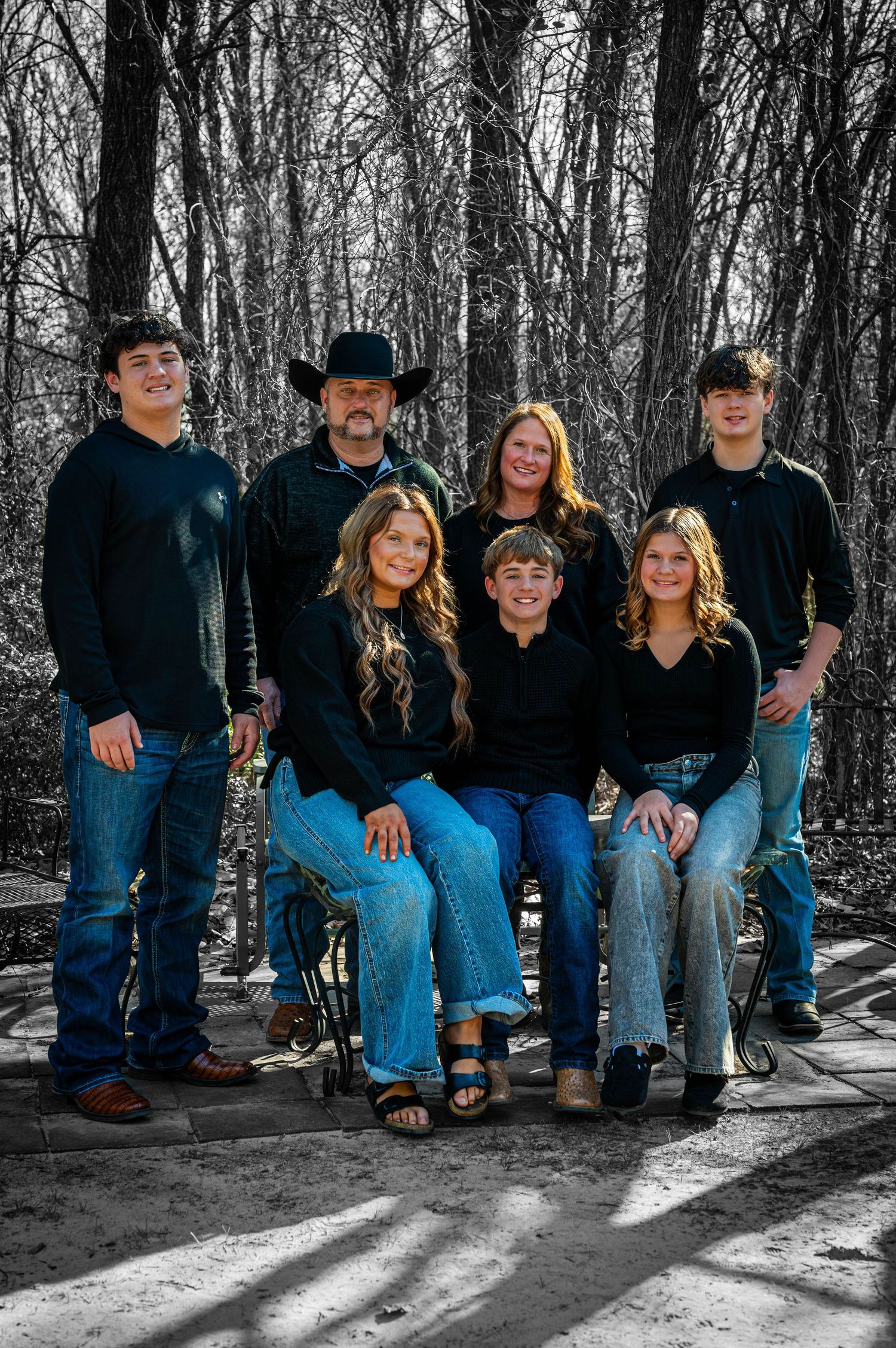 A group sits together on a wooden bench in a forest setting wearing coordinated blue jeans and dark tops.