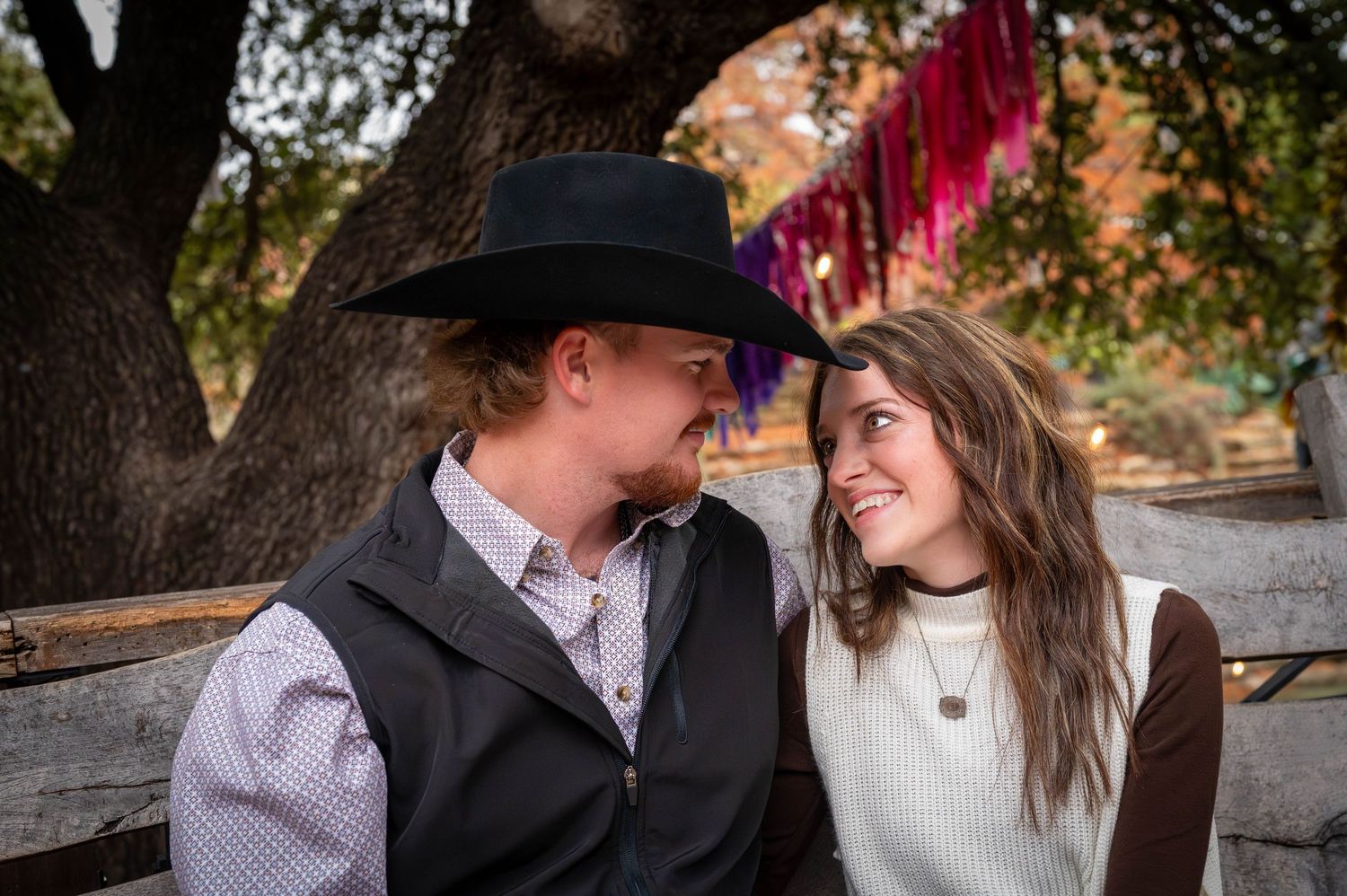 A romantic couple in western attire share intimate moments during a rustic outdoor engagement photo session at sunset.