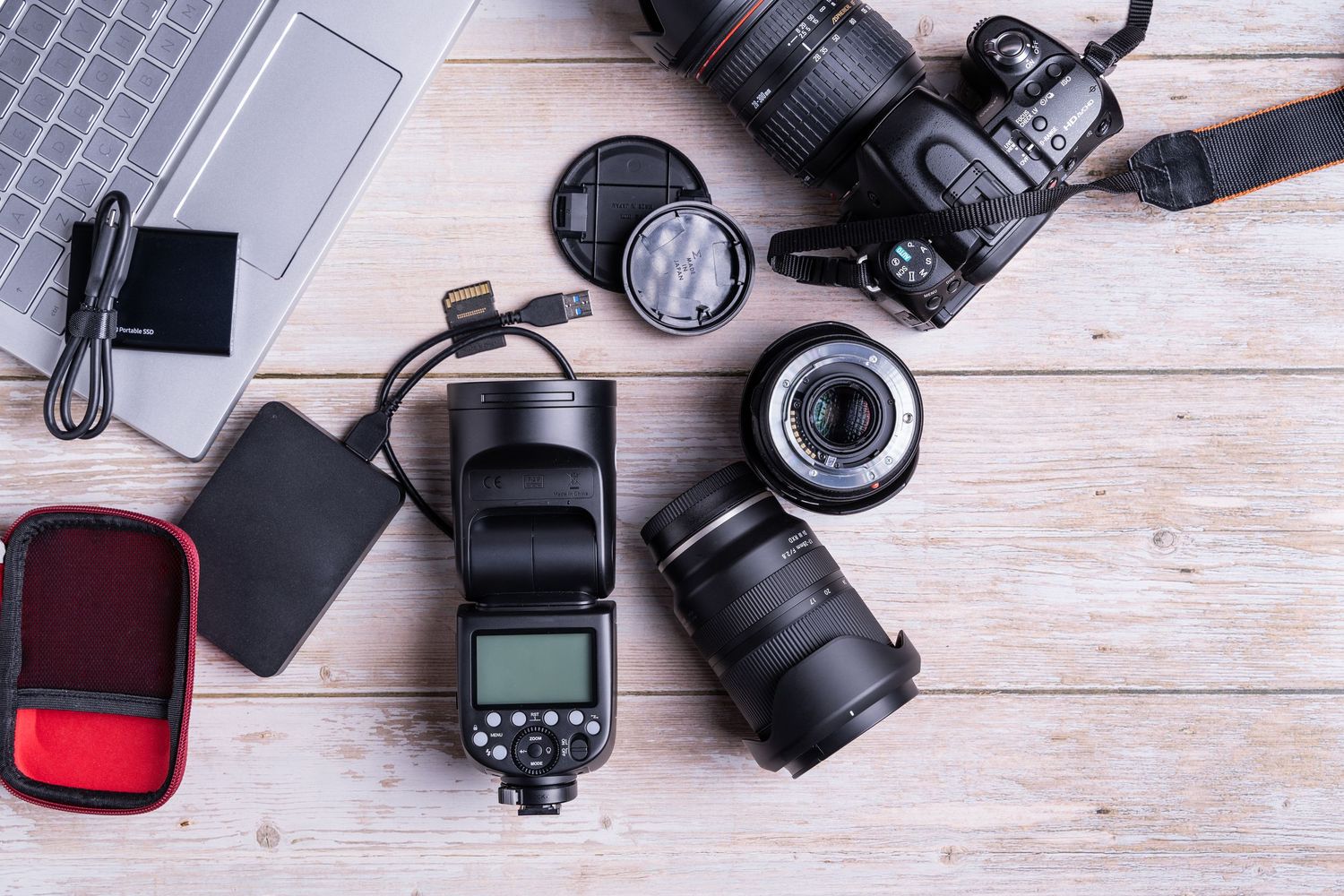 Professional photography equipment including cameras, lenses, and flashes laid out on a white wooden surface.