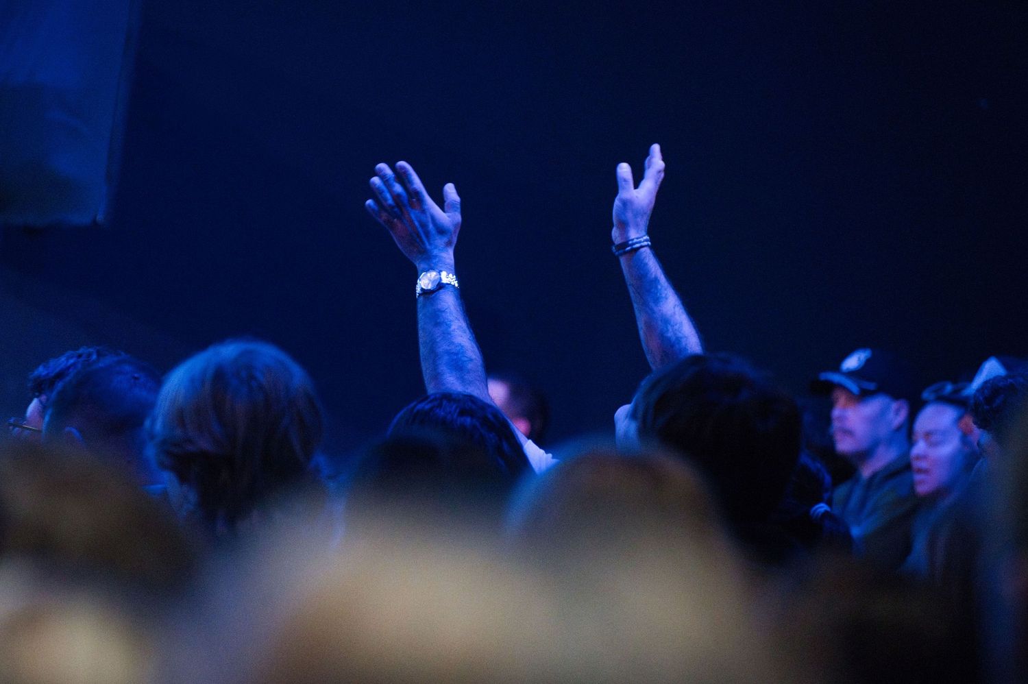 Church crowd with raised hands silhouetted against dramatic blue stage lighting during worship.