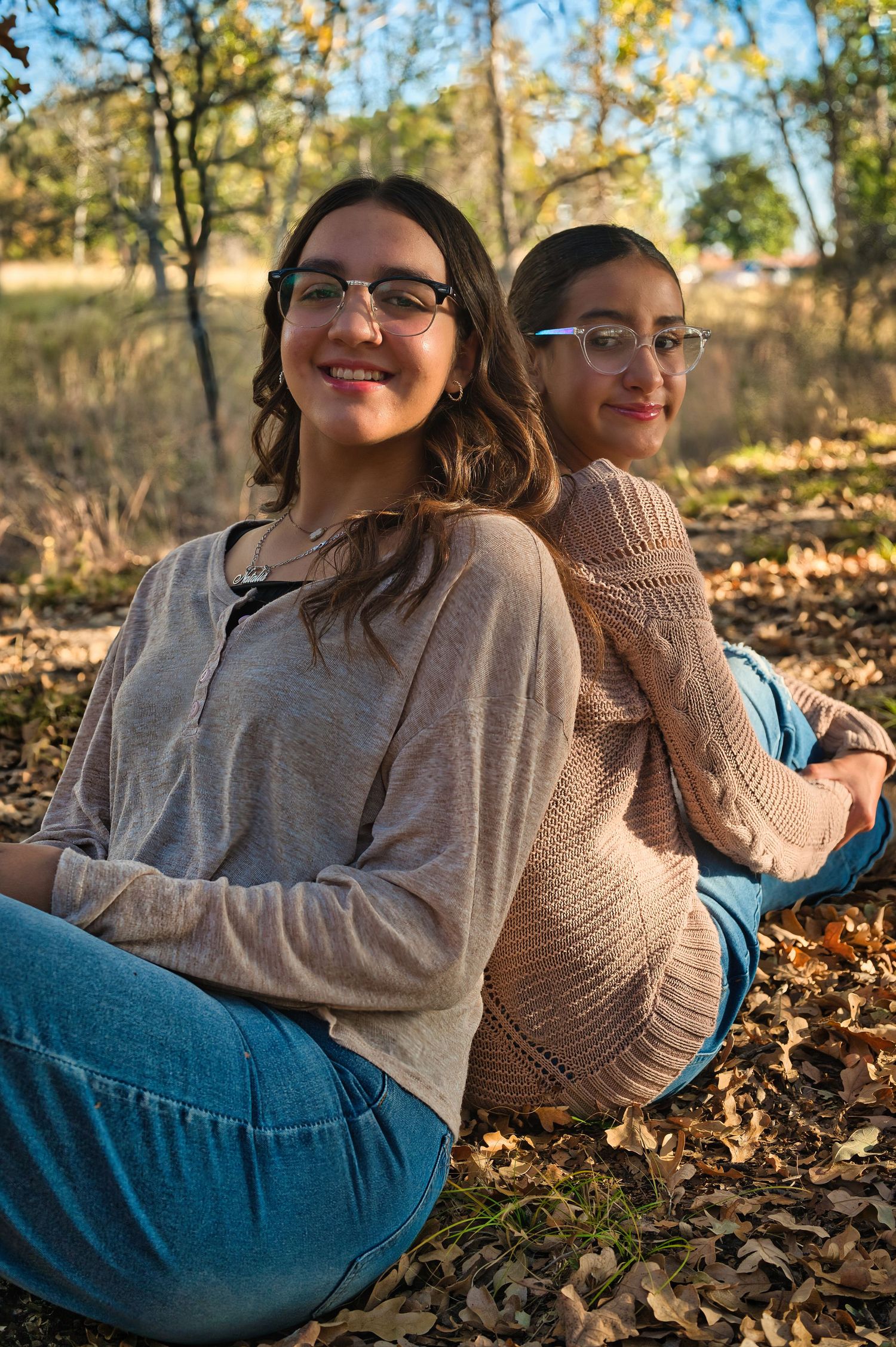 Person in beige sweater and blue jeans relaxes on autumn leaves during golden hour photo session. Azle family photo session.
