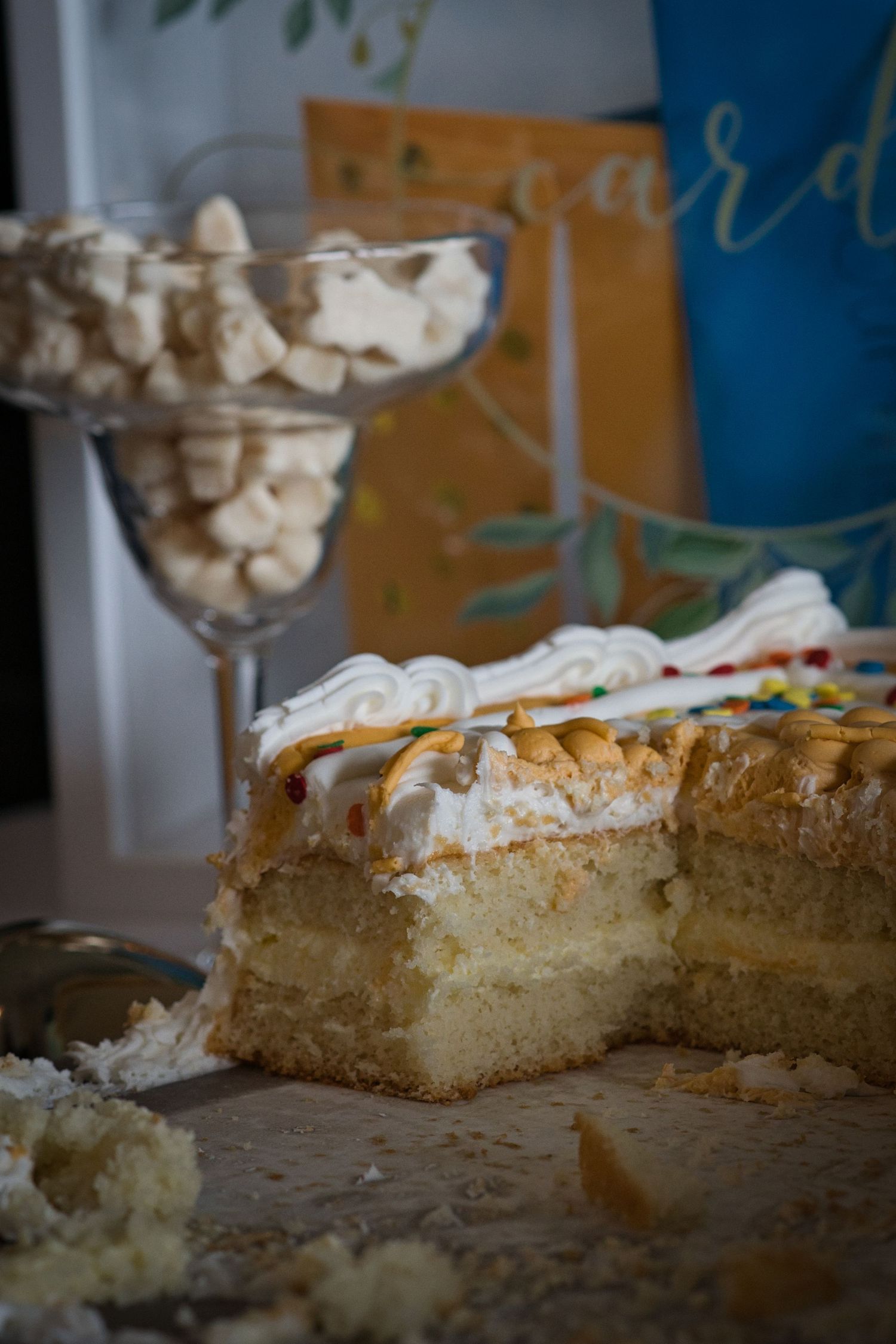 Sliced white layer cake with whipped cream topping and crumbs on a dark surface shown from multiple angles.