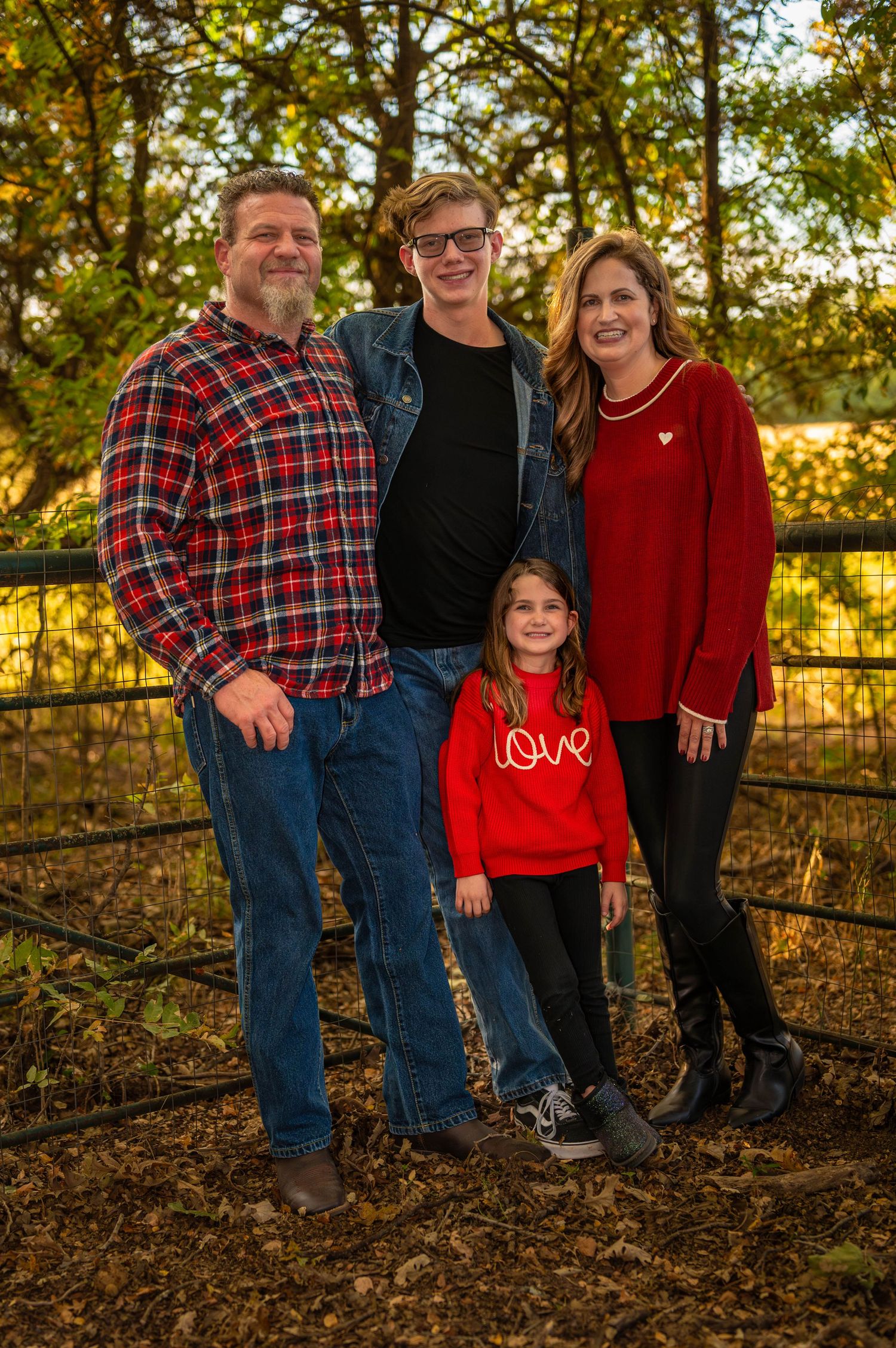 Family poses together in autumn setting with fallen leaves and rustic fence at golden hour sunset. Azle family photo session.