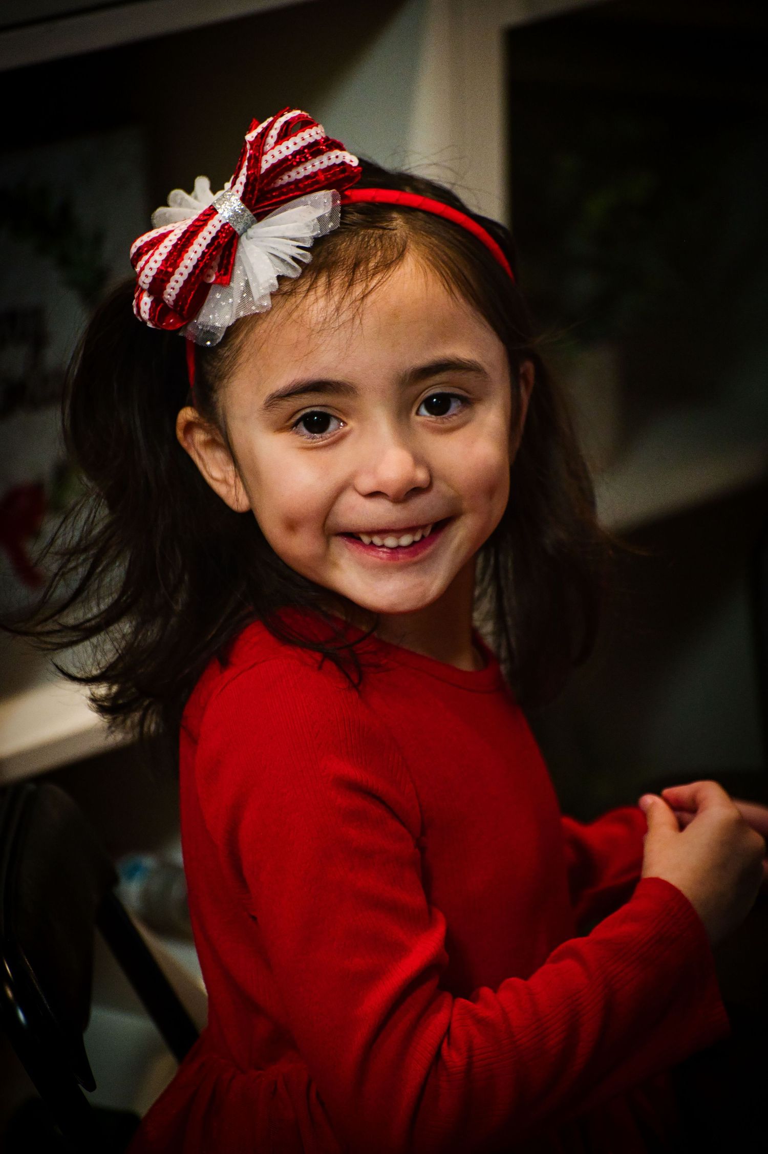 A series of photos showing a child in a red sweater and festive bow headband smiling and turning playfully.