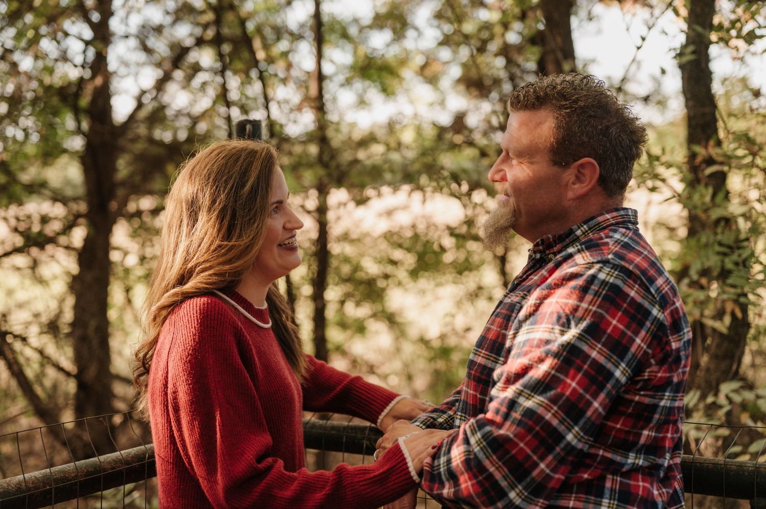 A couple in red plaid shirts shares a romantic moment outdoors among trees during golden hour. Azle family photo session.