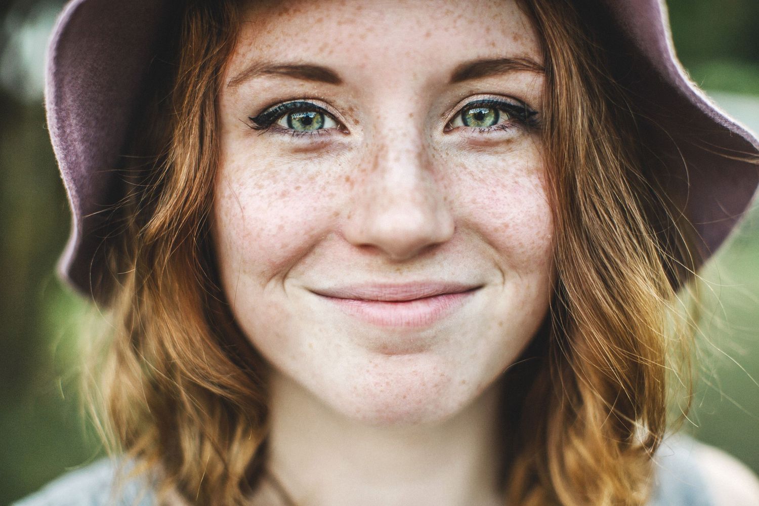 A series of headshots showing someone with red hair and freckles smiling warmly at the camera in an outdoor setting.