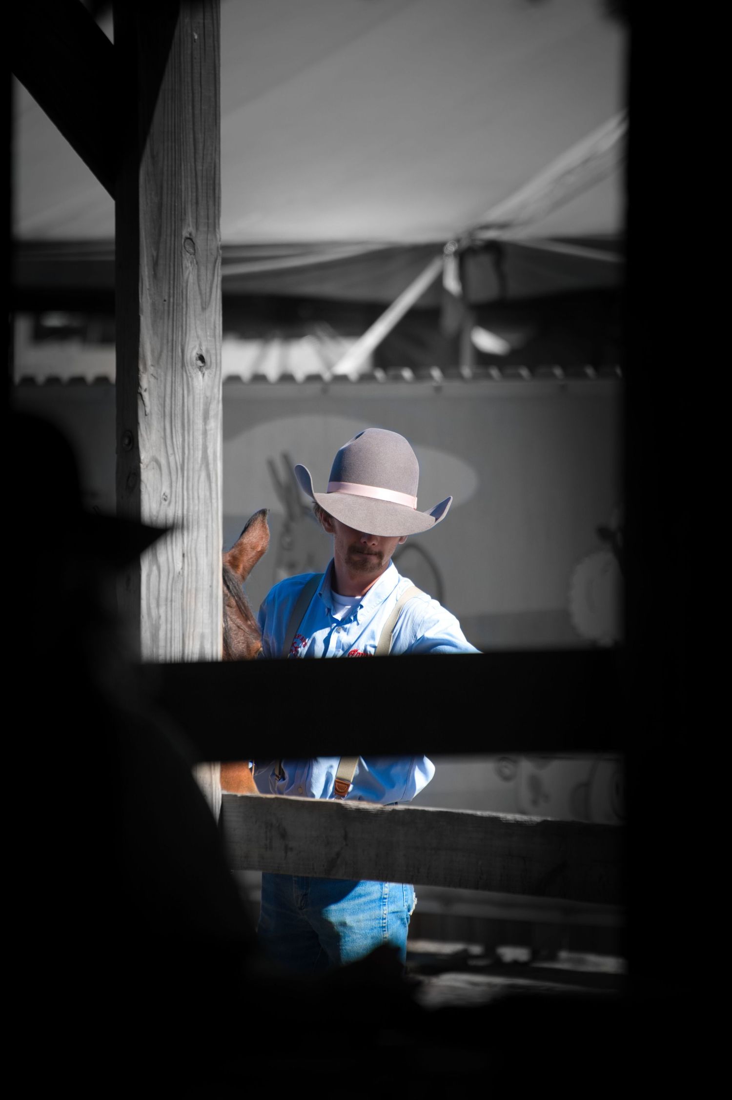 A person in a blue shirt and cowboy hat is seen through wooden beams in a black and white photograph.