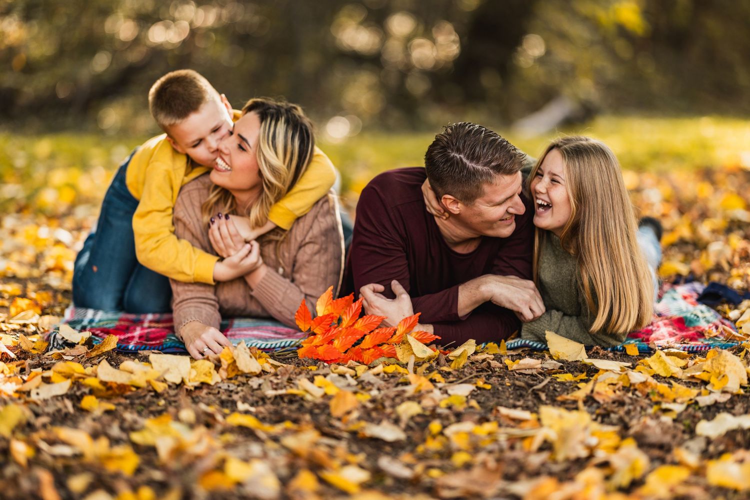 Couple shares romantic moments while laying on colorful autumn leaves in a park during golden hour.