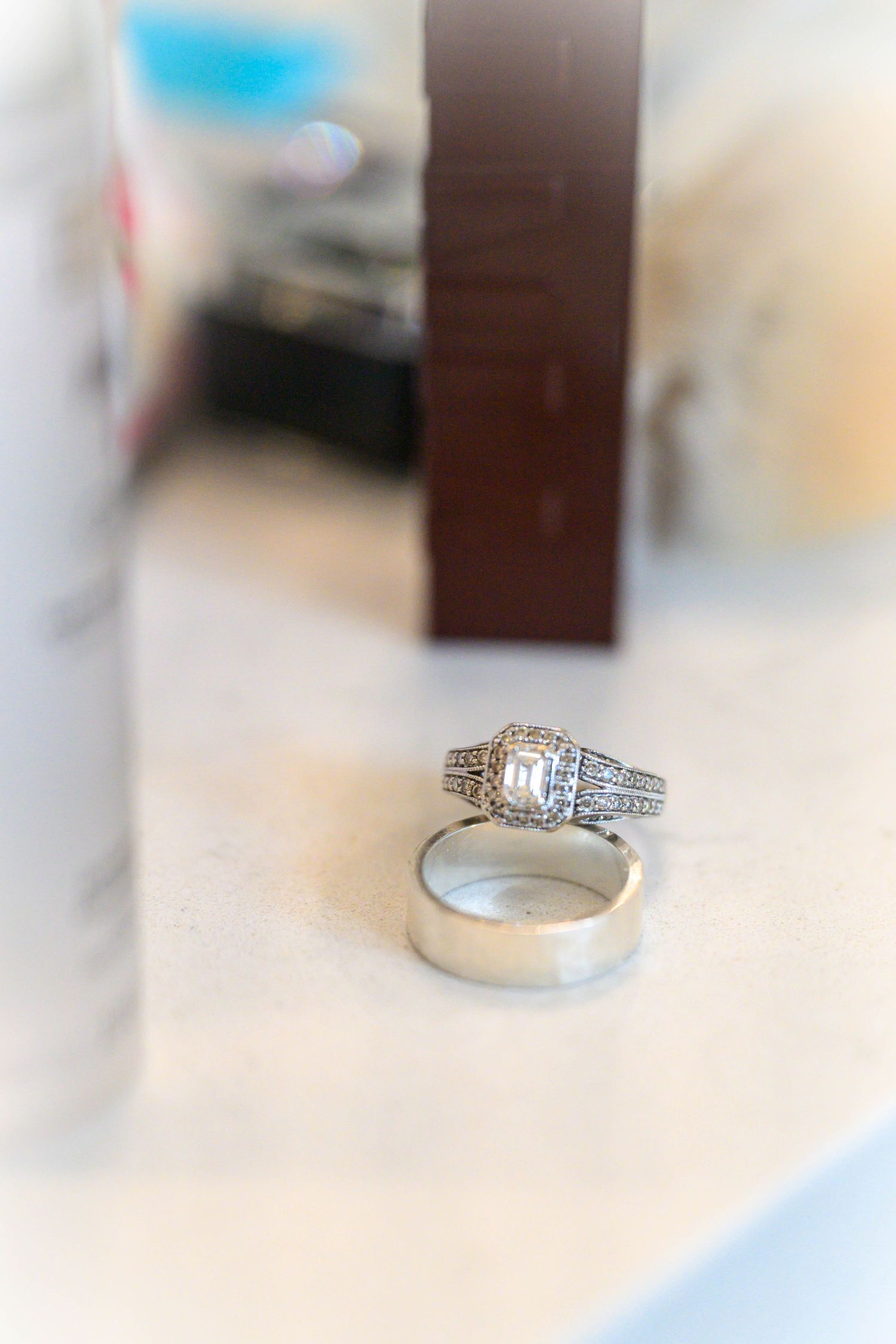 Diamond halo engagement ring stacked on a plain silver wedding band displayed on a white surface.