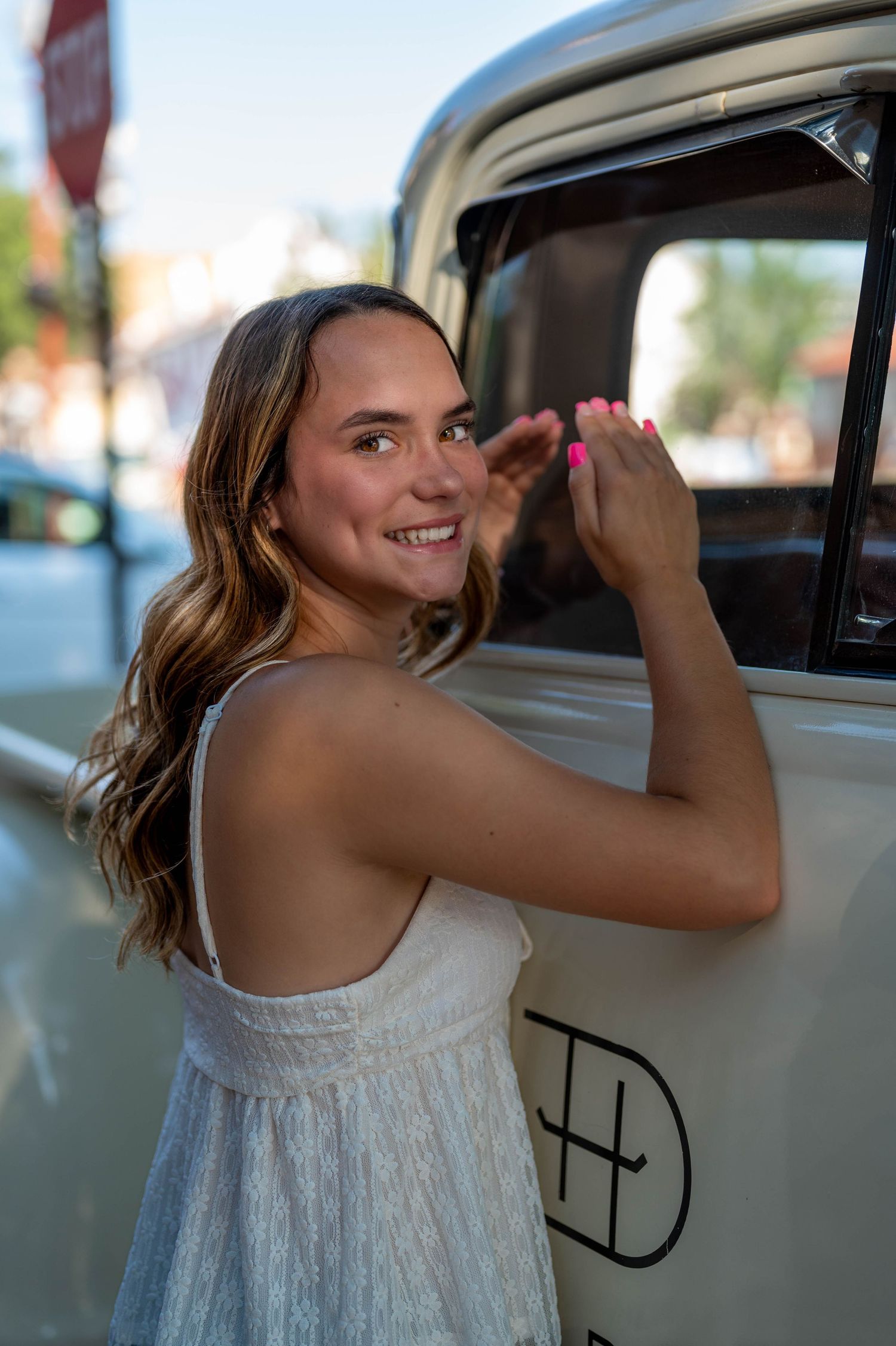 Woman in white dress smiles while looking through car window on sunny day. Azle senior at the fort worth stockyards.