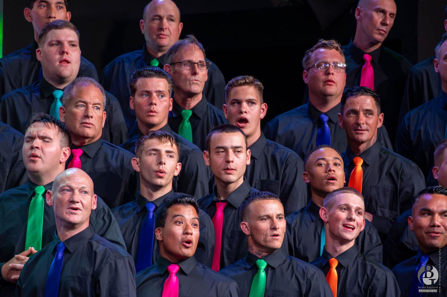 A choir group of men wearing colorful ties performs together in a formal arrangement.