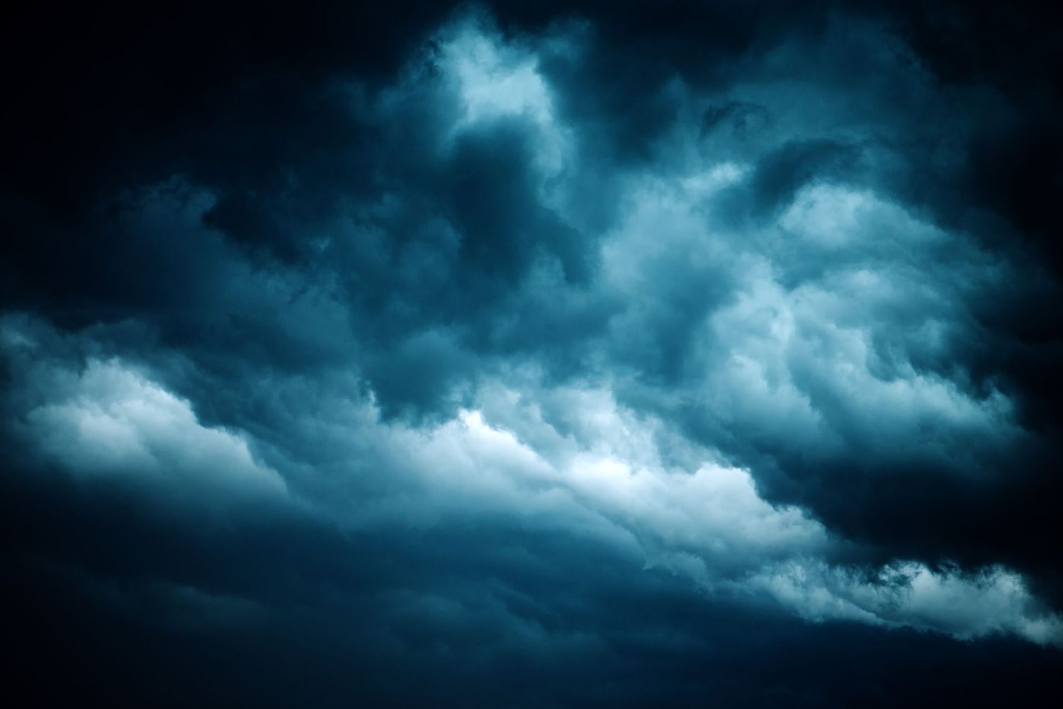 Dark stormy clouds with dramatic blue and teal hues fill the sky, creating an ominous and powerful weather scene.