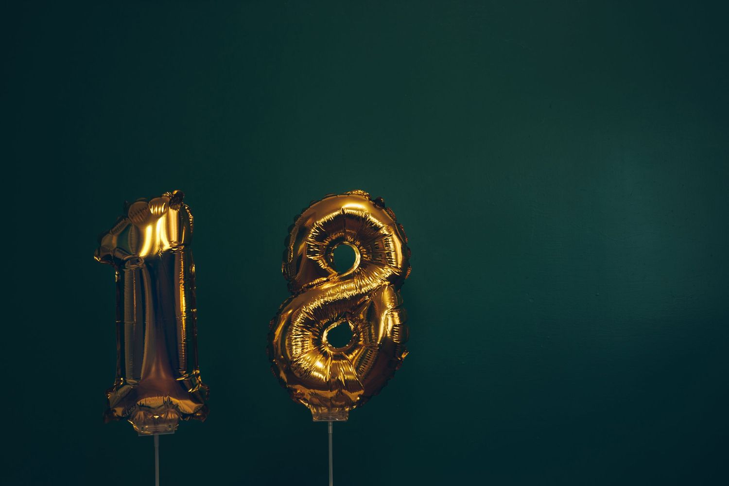 Gold foil balloons shaped as the number 18 against a dark green background, perfect for an eighteenth birthday celebration.