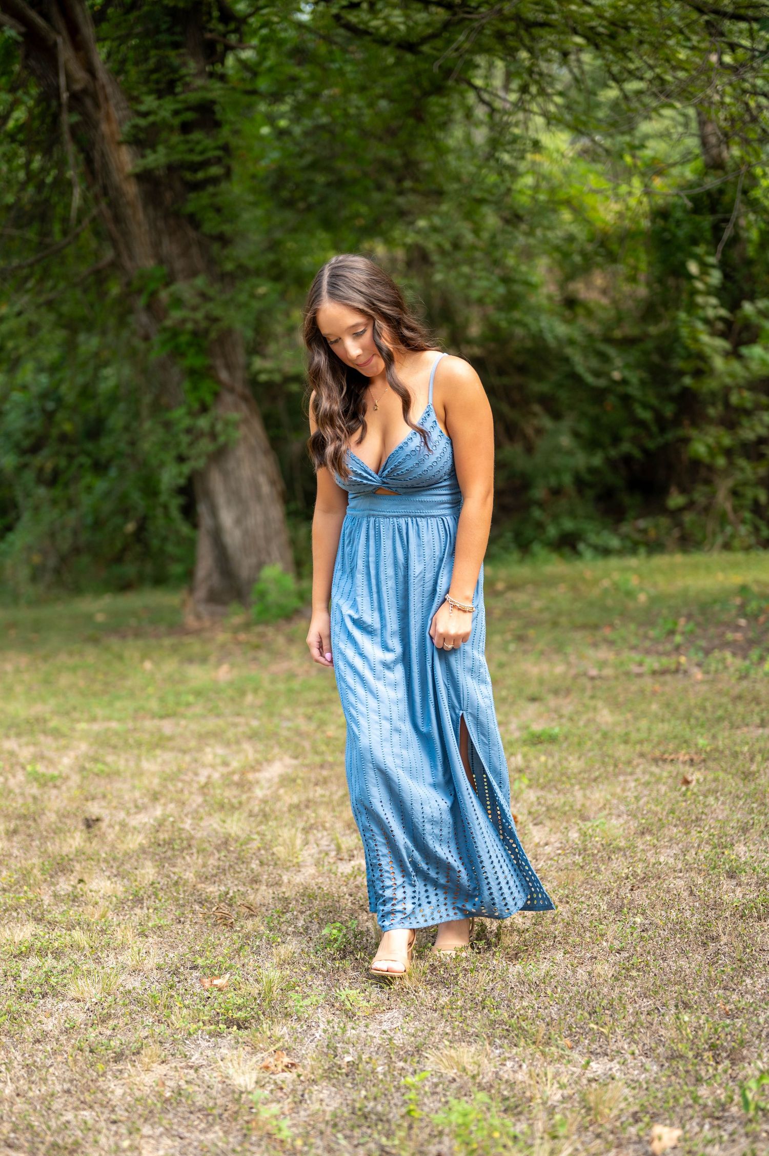 Photos showing a senior in a flowing blue summer dress walking through a grassy outdoor area. Azle senior photo session.