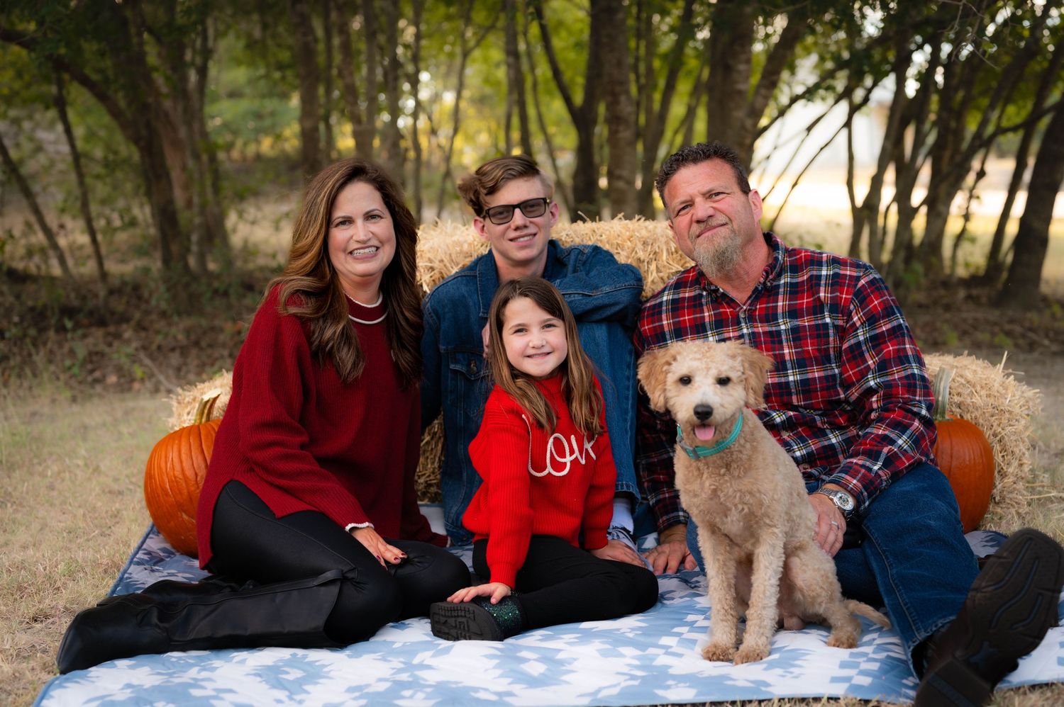 A family and their dog pose together outdoors in coordinating red and navy outfits during a photo session. Azle family photo session.