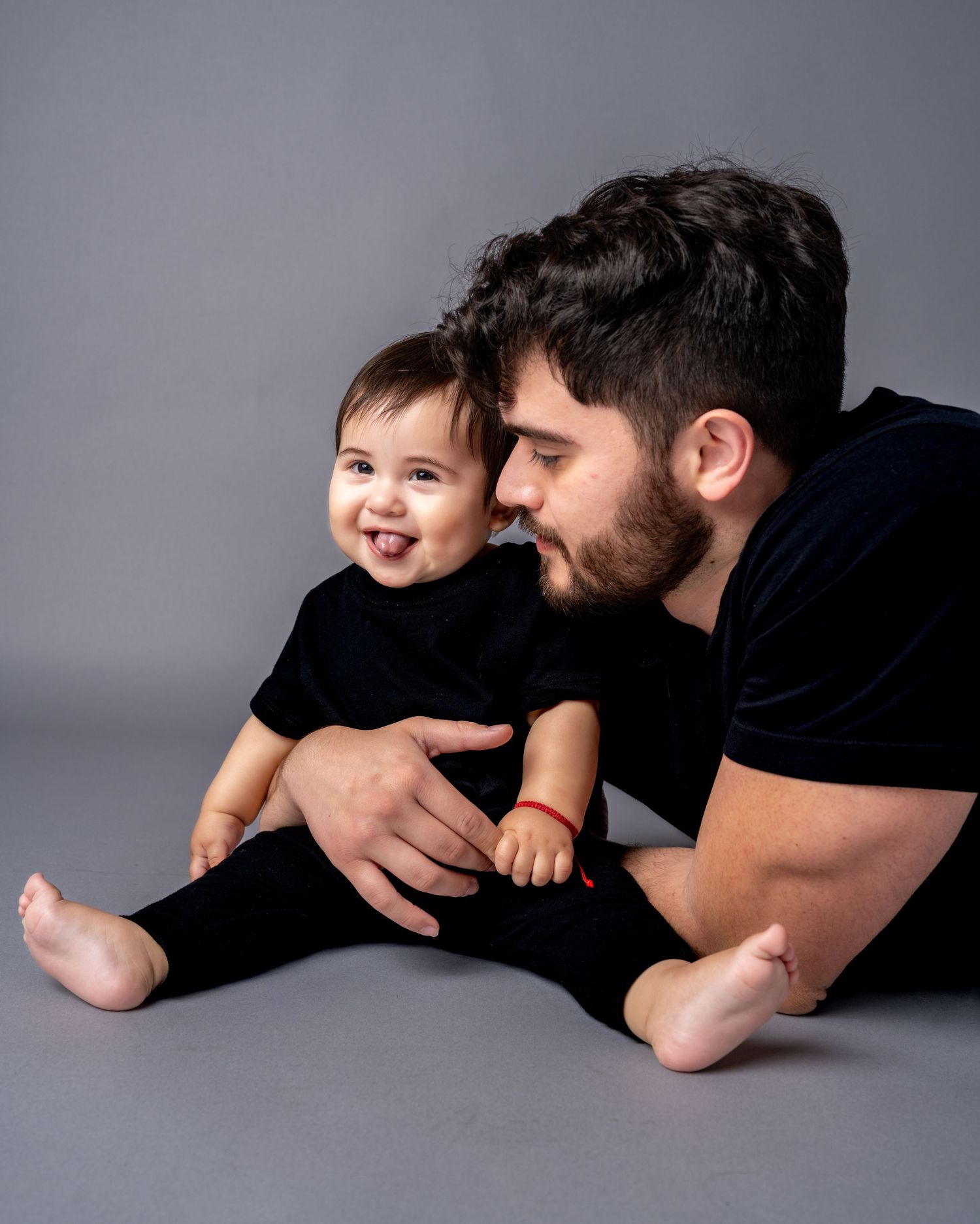 A tender moment between parent and child lying on a grey backdrop in a series of black and white studio portraits.