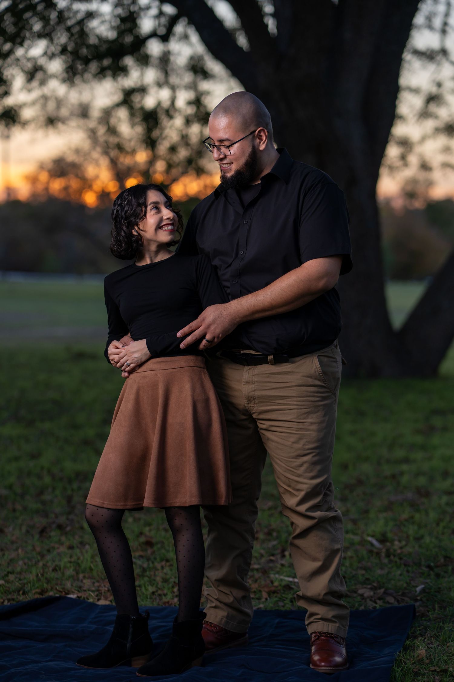 A couple shares an intimate moment at sunset on a blanket in a grassy field.