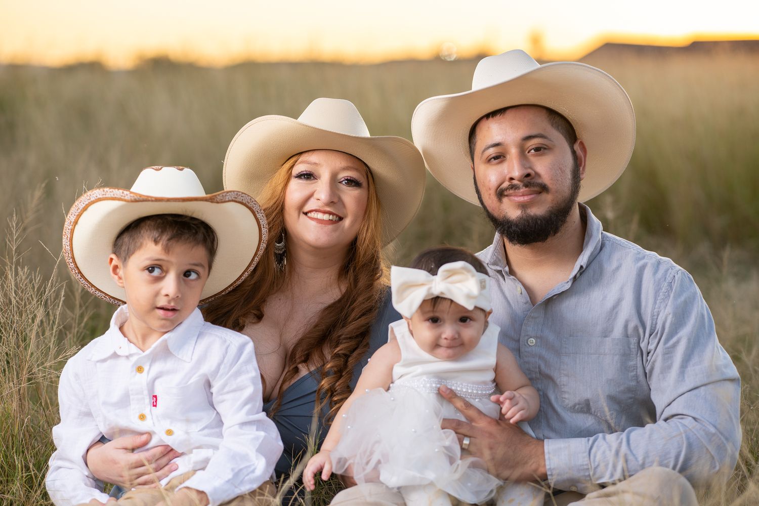 Family Photograph of a family of four wearing cowboy hats sitting together in a sunlit field during golden hour.