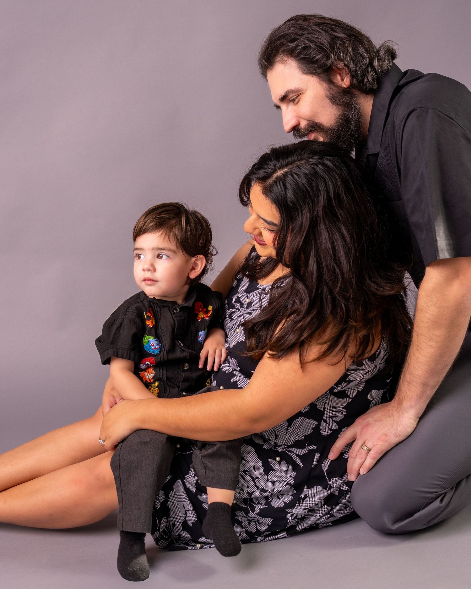 Family studio portrait with parents and child sitting together against a gray background.