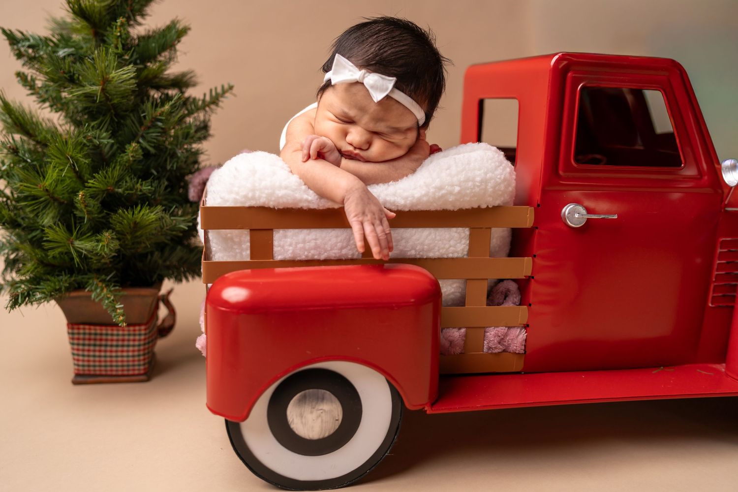 Christmas themed newborn photography setup with vintage red truck and evergreen decorations.
