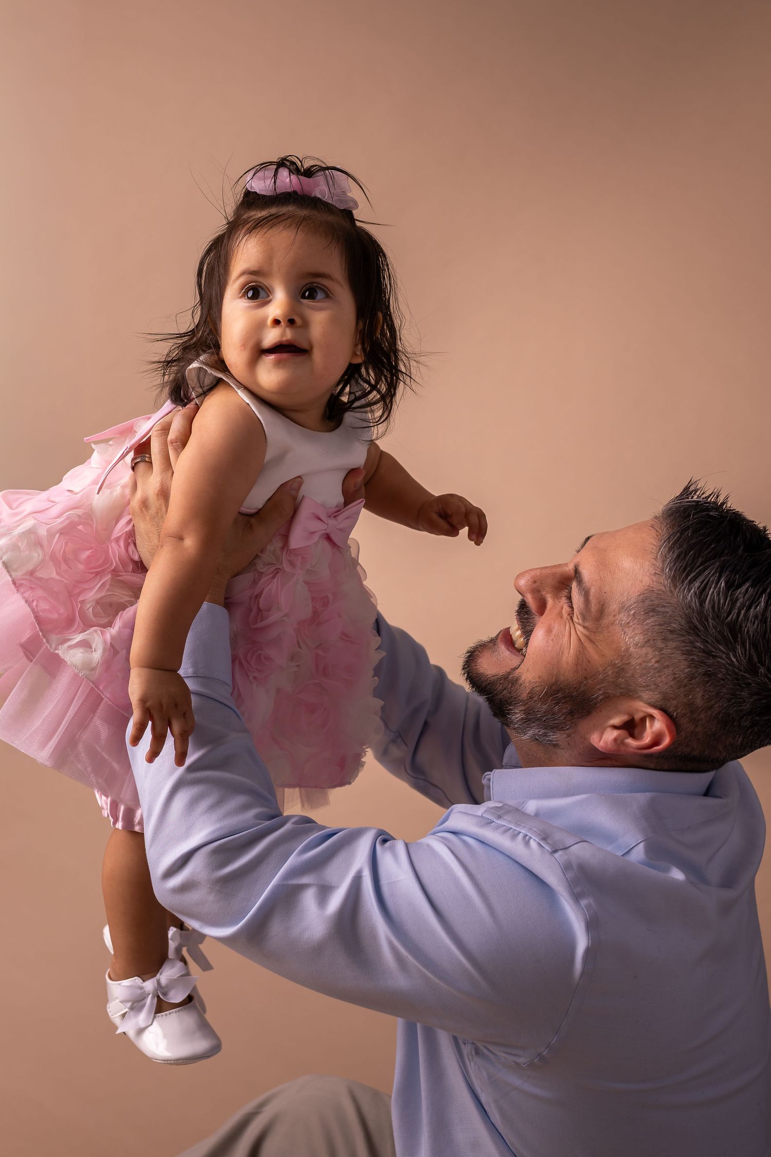 A sequence of playful interactions between parent and child in pink and blue clothing against beige background.