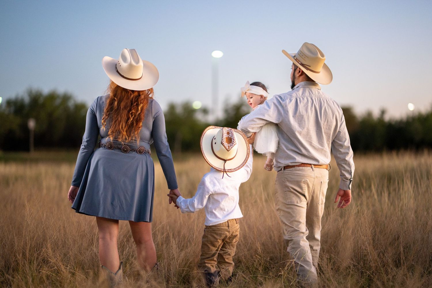 Family in casual attire walking together through a golden field at sunset holding hands.