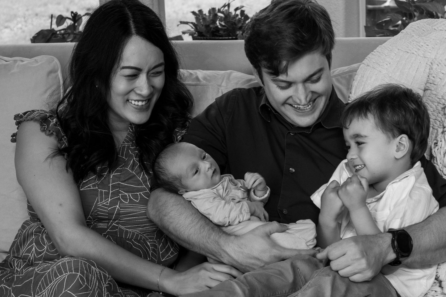 Happy family with newborn baby and toddler smiling together on a couch.