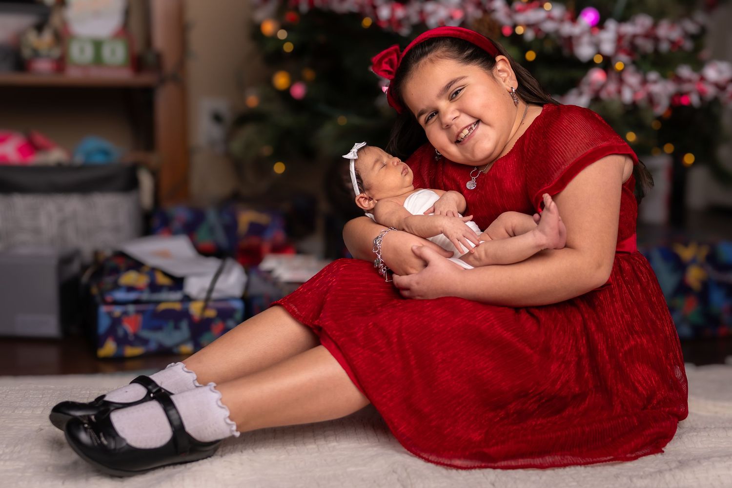 A person in a red dress lies on the floor next to Christmas decorations during a holiday photo session.
